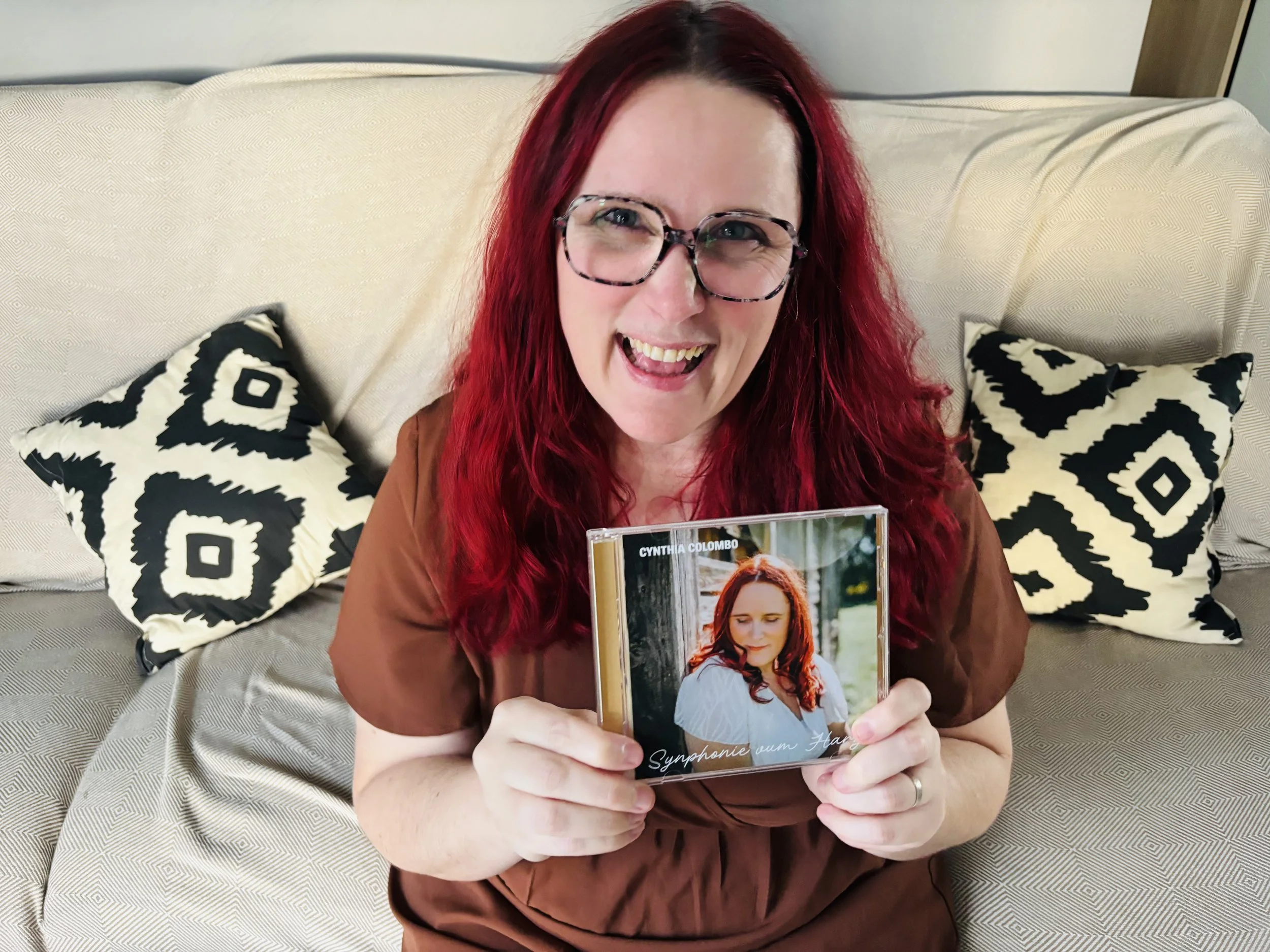 Une femme aux cheveux rouge, souriante, joyeuse, qui tiens un CD dans la main