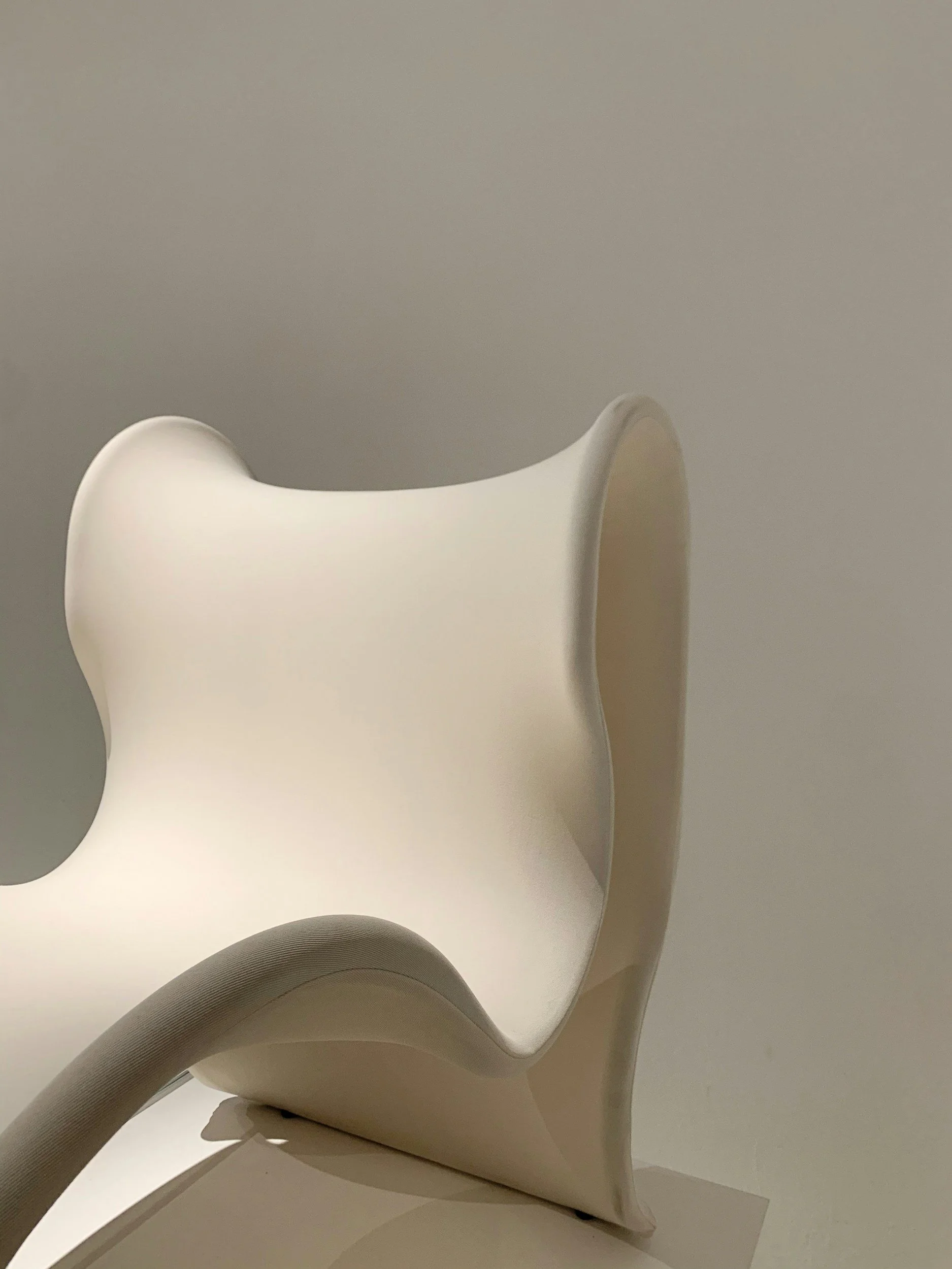 Close-up of a modern, white, plastic chair with smooth, curved design against a plain gray background.