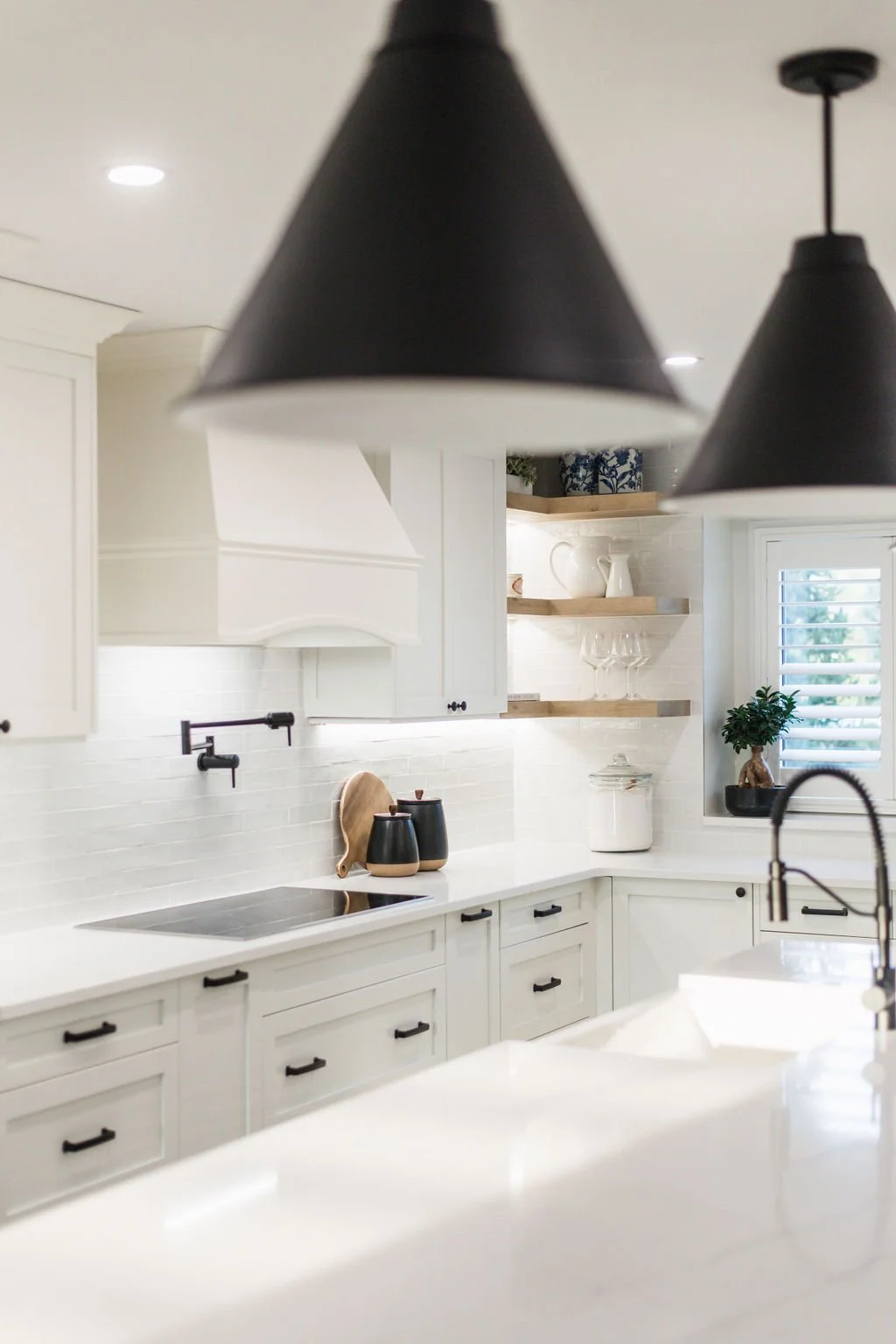 Modern white kitchen with black handles, open shelves, and black pendant lights