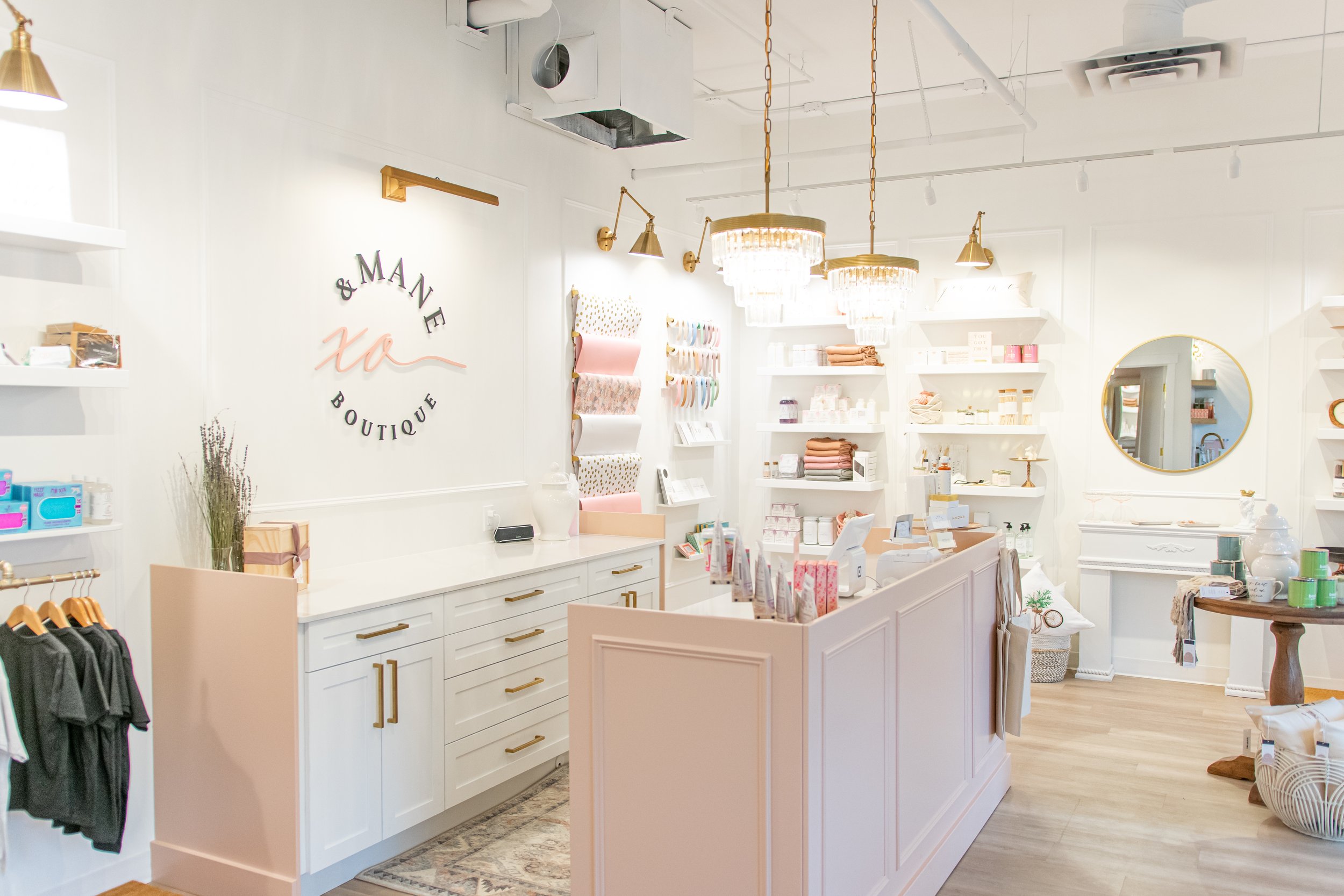 Interior of a boutique store with white walls and shelves, displaying various products, a pink counter, and decorative lighting fixtures