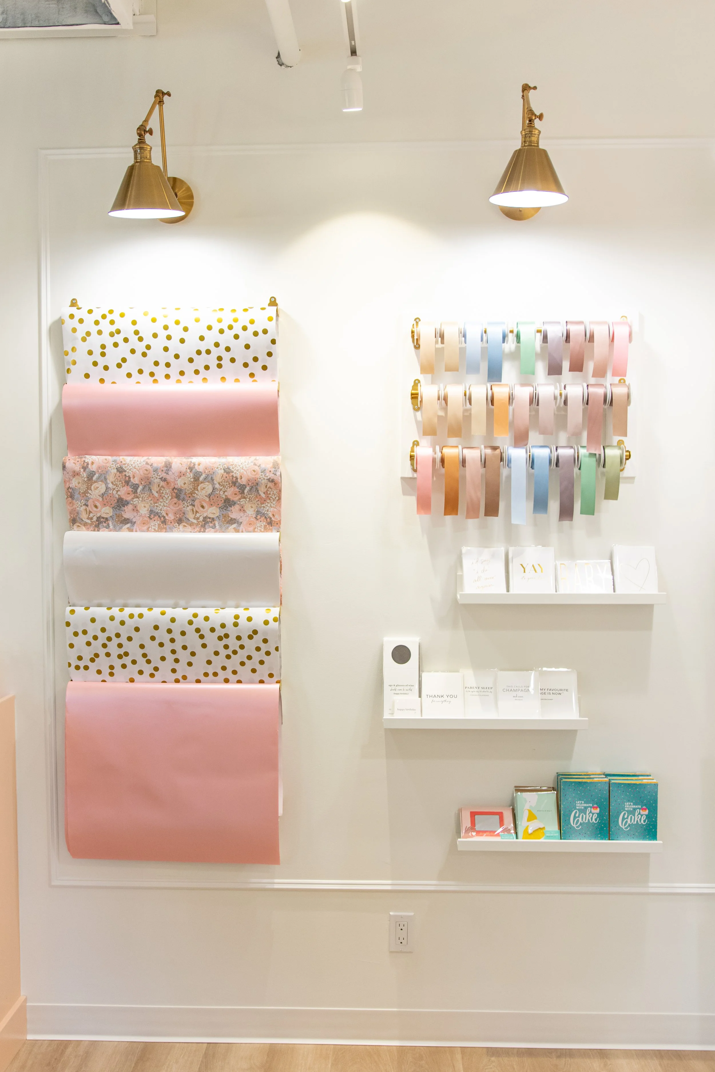 Display of decorative wrapping paper rolls on the wall and shelves with greeting cards and gift boxes in a store.