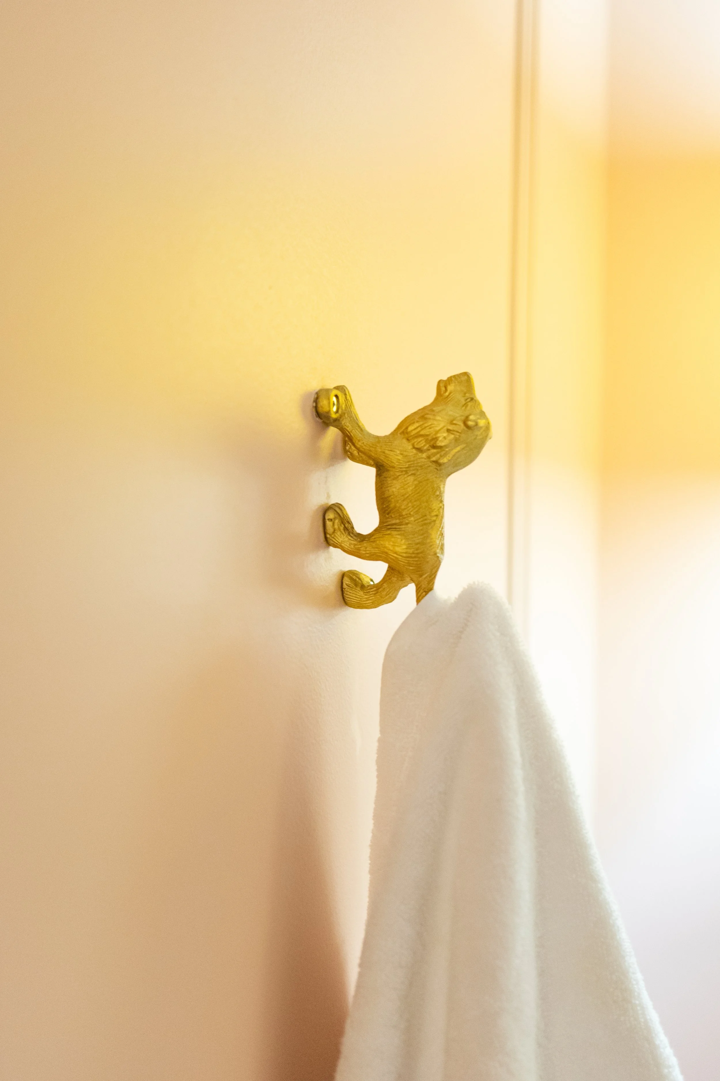 Gold bear-shaped towel hook with a white towel hanging on it, mounted on a yellow wall.