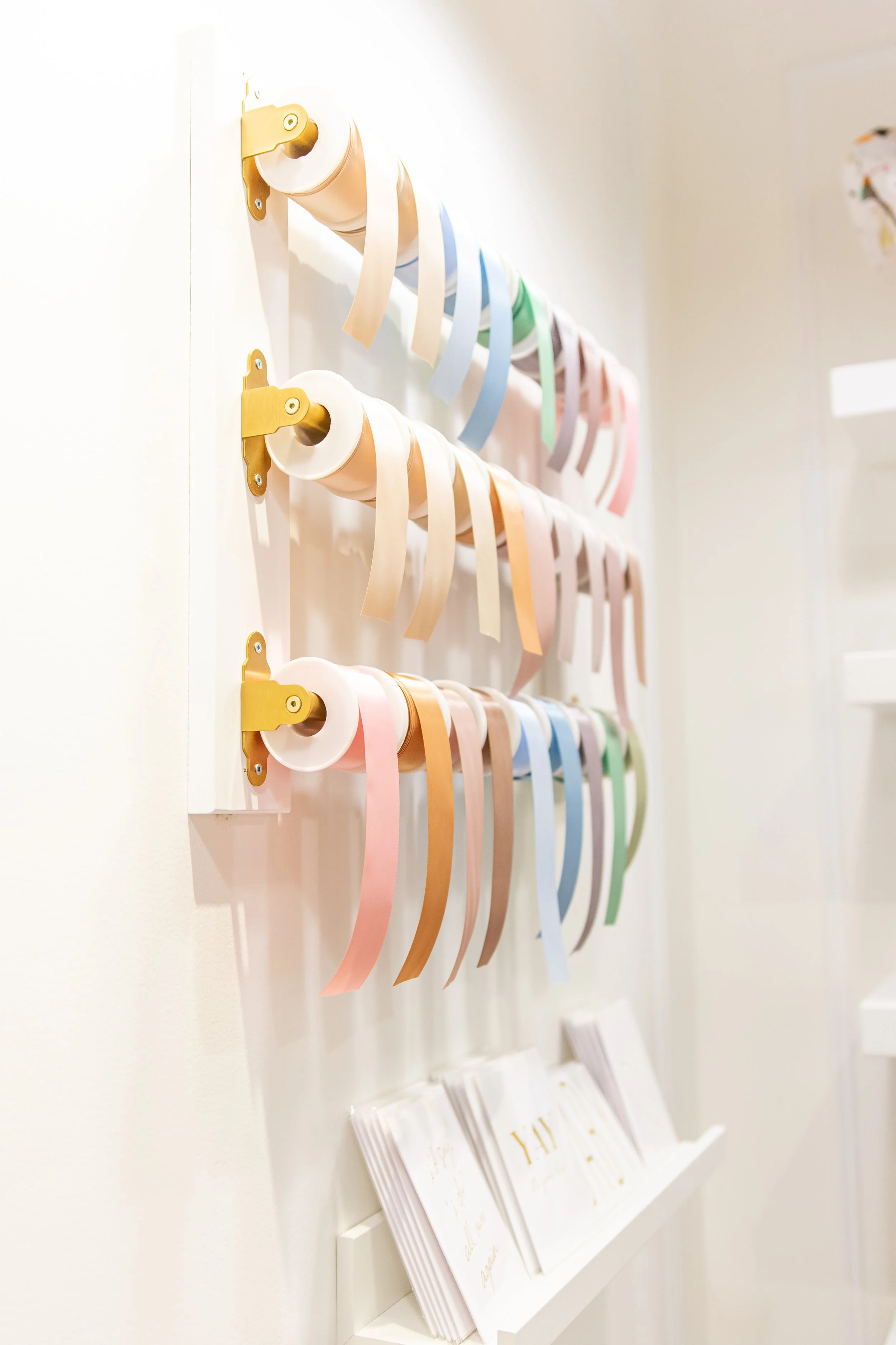 Display of pastel-colored ribbons on wall hooks in a craft or boutique setting.