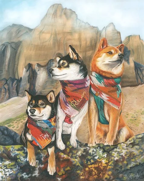 Three dogs with bandanas sit outdoors in front of mountain scenery.