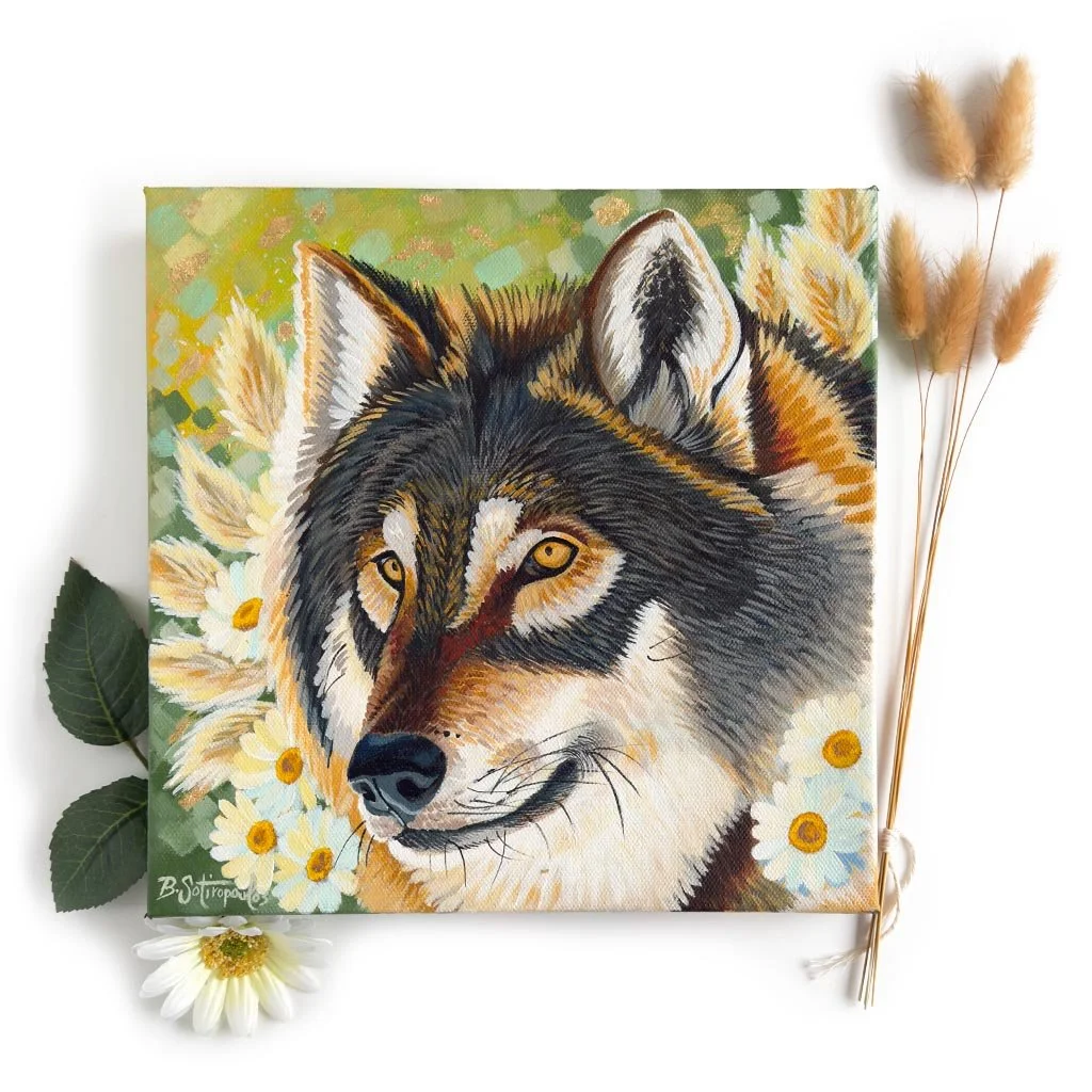 Painted portrait of a wolf surrounded by daisies and greenery, with dried pampas grass and a white daisy arranged around the artwork.