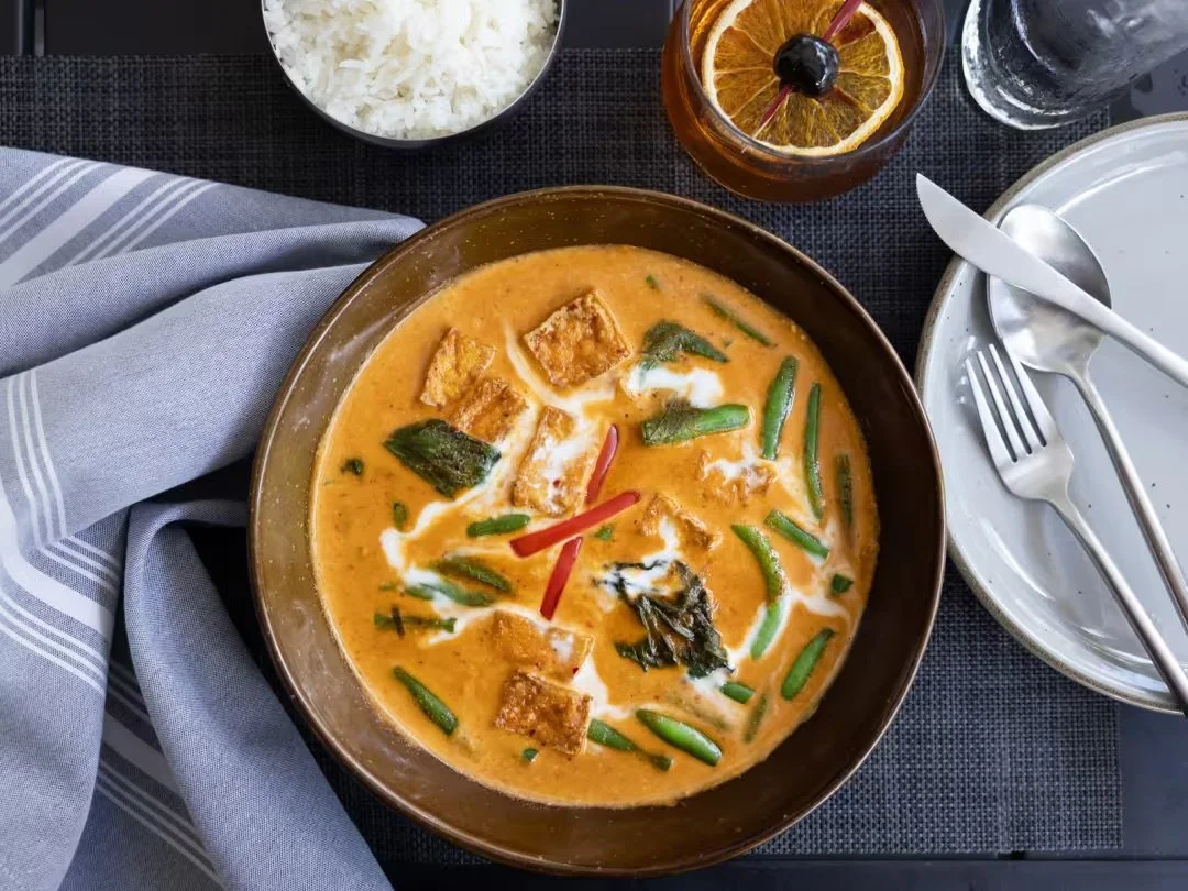 Thai curry dish at 26 Thai Kitchen & Bar in Midtown Atlanta served with vegetables, tofu, rice, and cocktail on a dining table