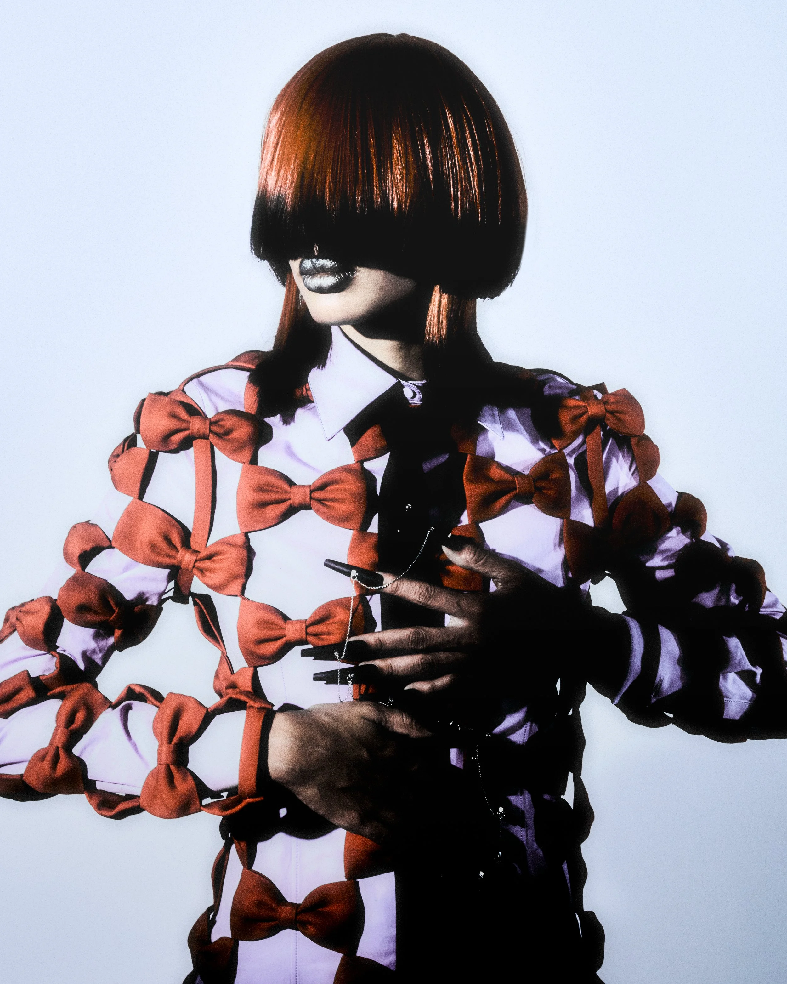 A woman with short, straight, bob haircut with bangs covering her eyes, wearing a white shirt decorated with numerous red bows, and holding a cellphone in her hand.