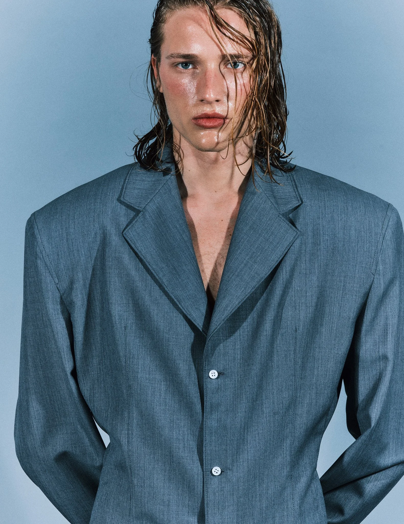 A woman with wet hair wearing a blue blazer against a plain background.