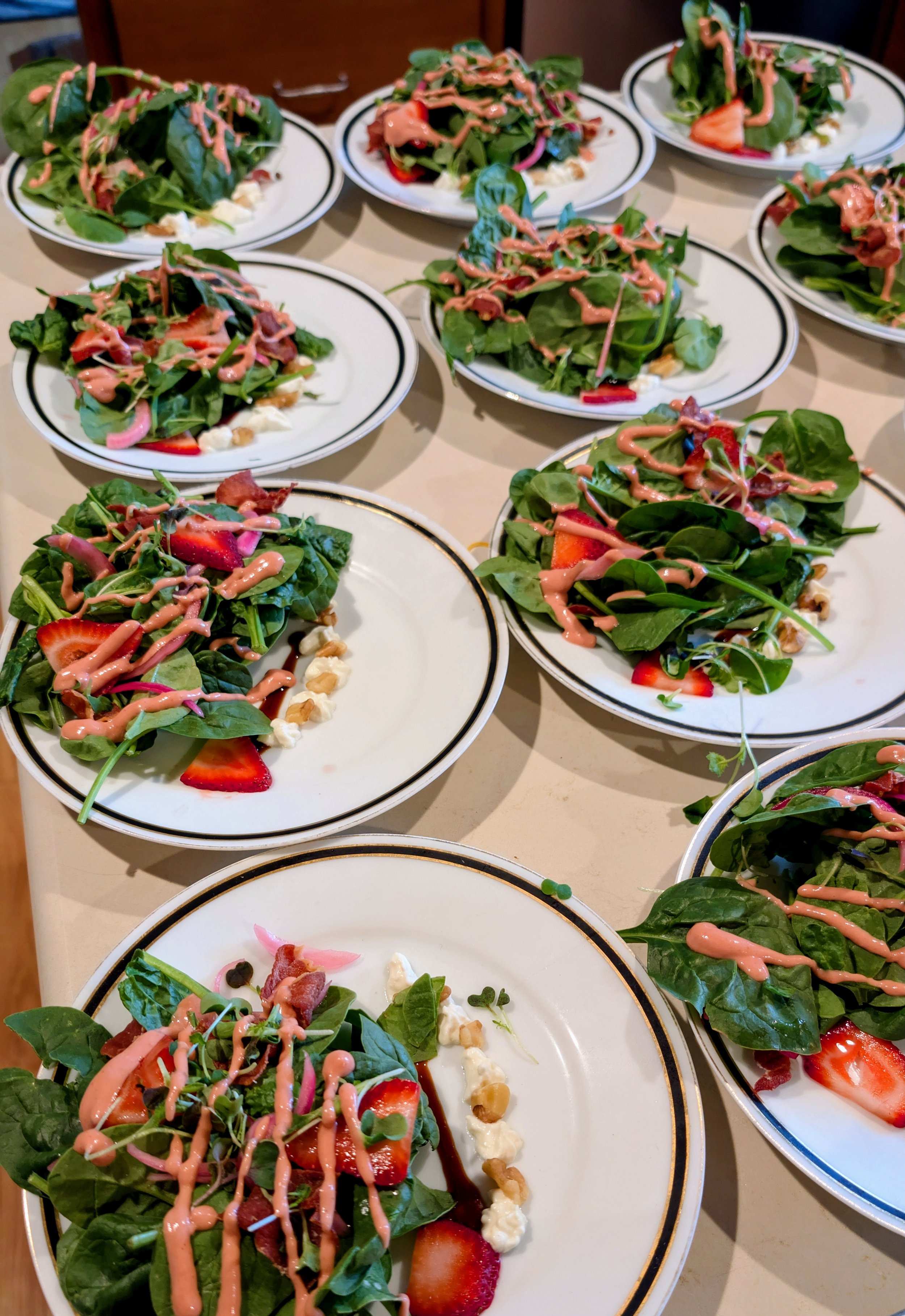 Several plates of fresh spinach salads with strawberries, bacon, nuts, topped with pink salad dressing.