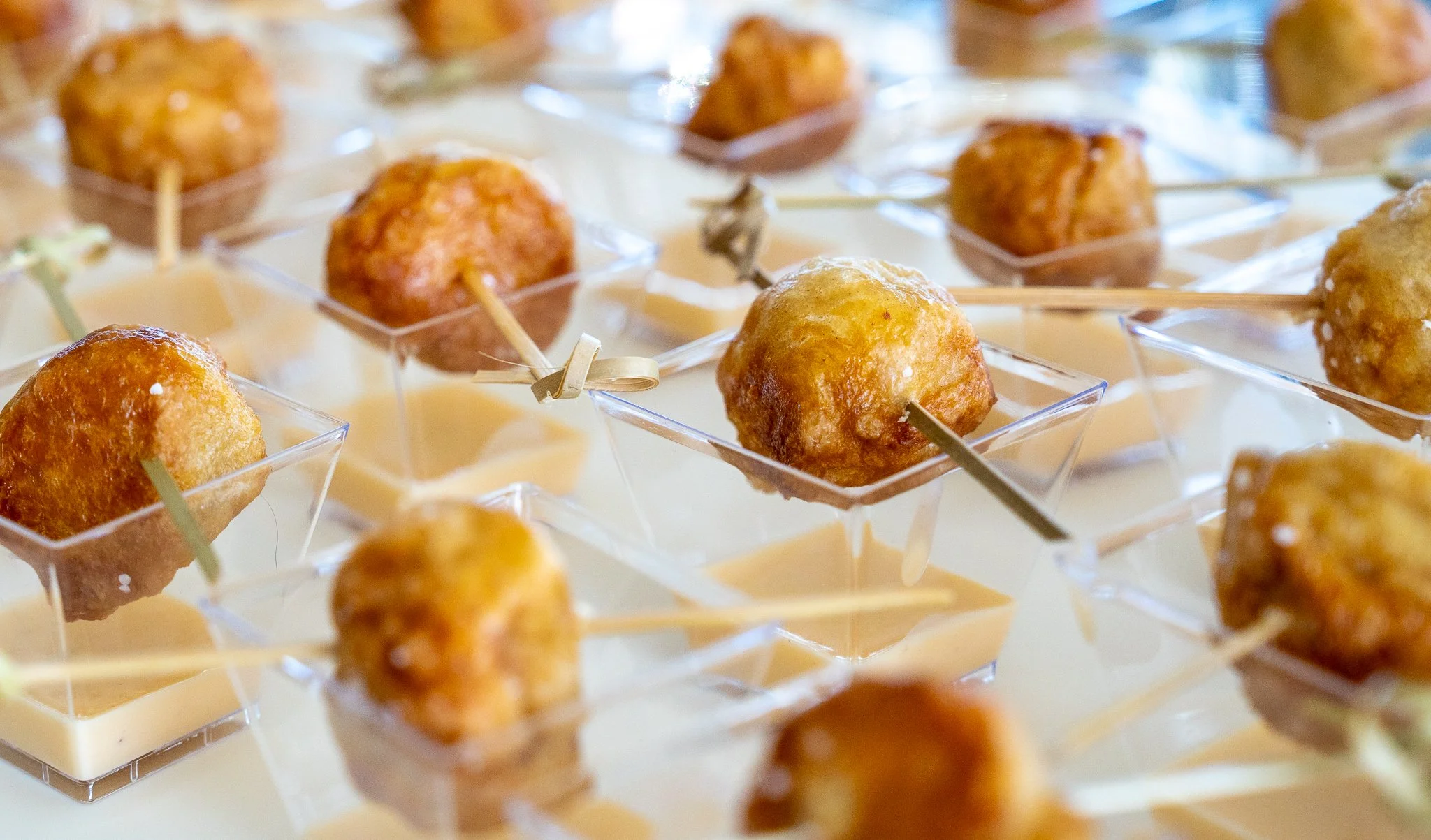 Close-up of chicken meatball appetizers on skewers served in small square glass dishes with creamy dipping sauce.
