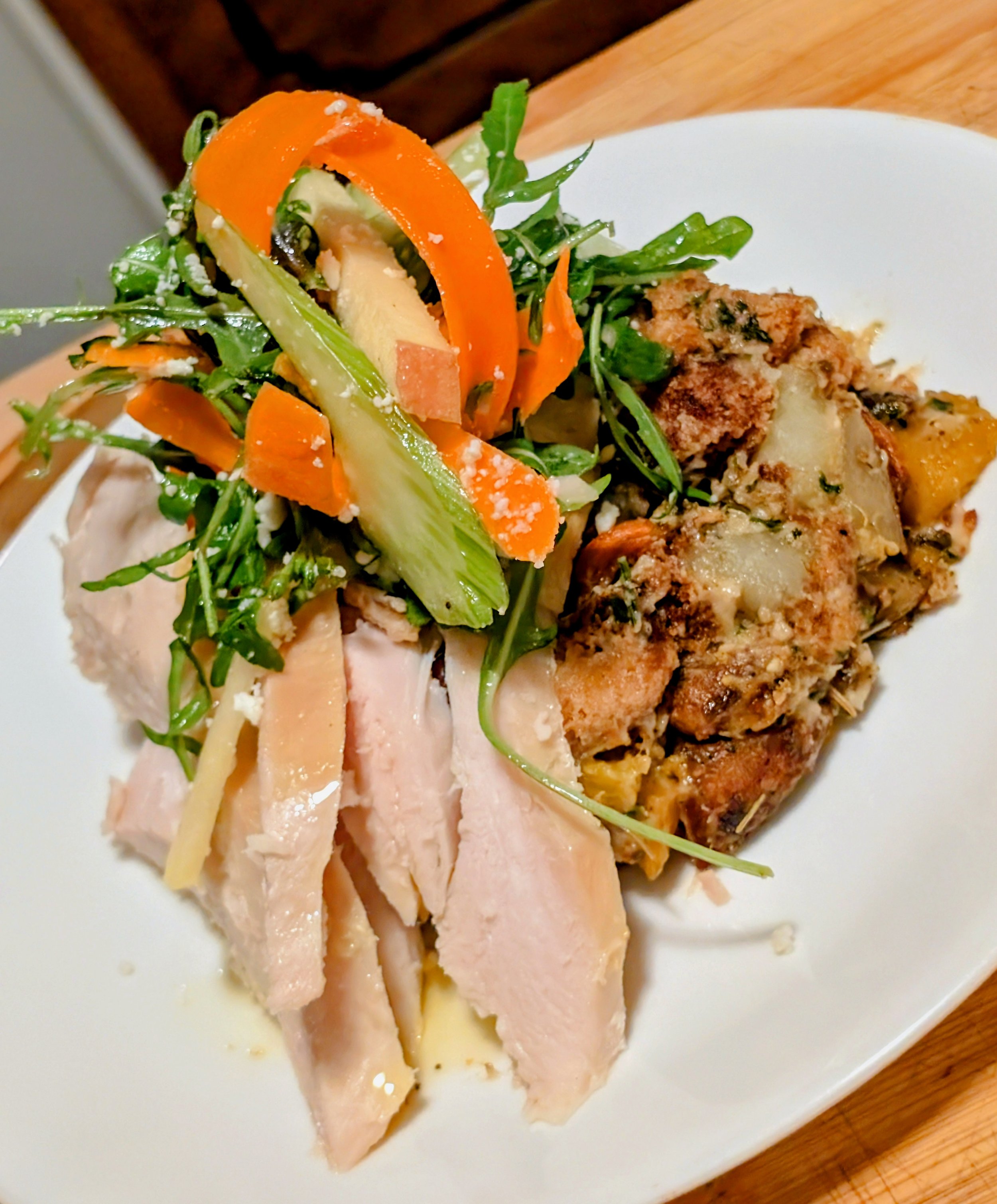 Plate with sliced turkey, a fresh vegetable salad with carrots, cucumbers, and greens, and a portion of baked dish with meat and cheese on a white oval plate.