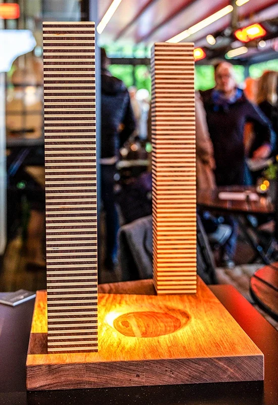 Zwei Holzmodelle mit gestreiftem Muster auf einer beleuchteten Holzbasis in einer belebten Umgebung.