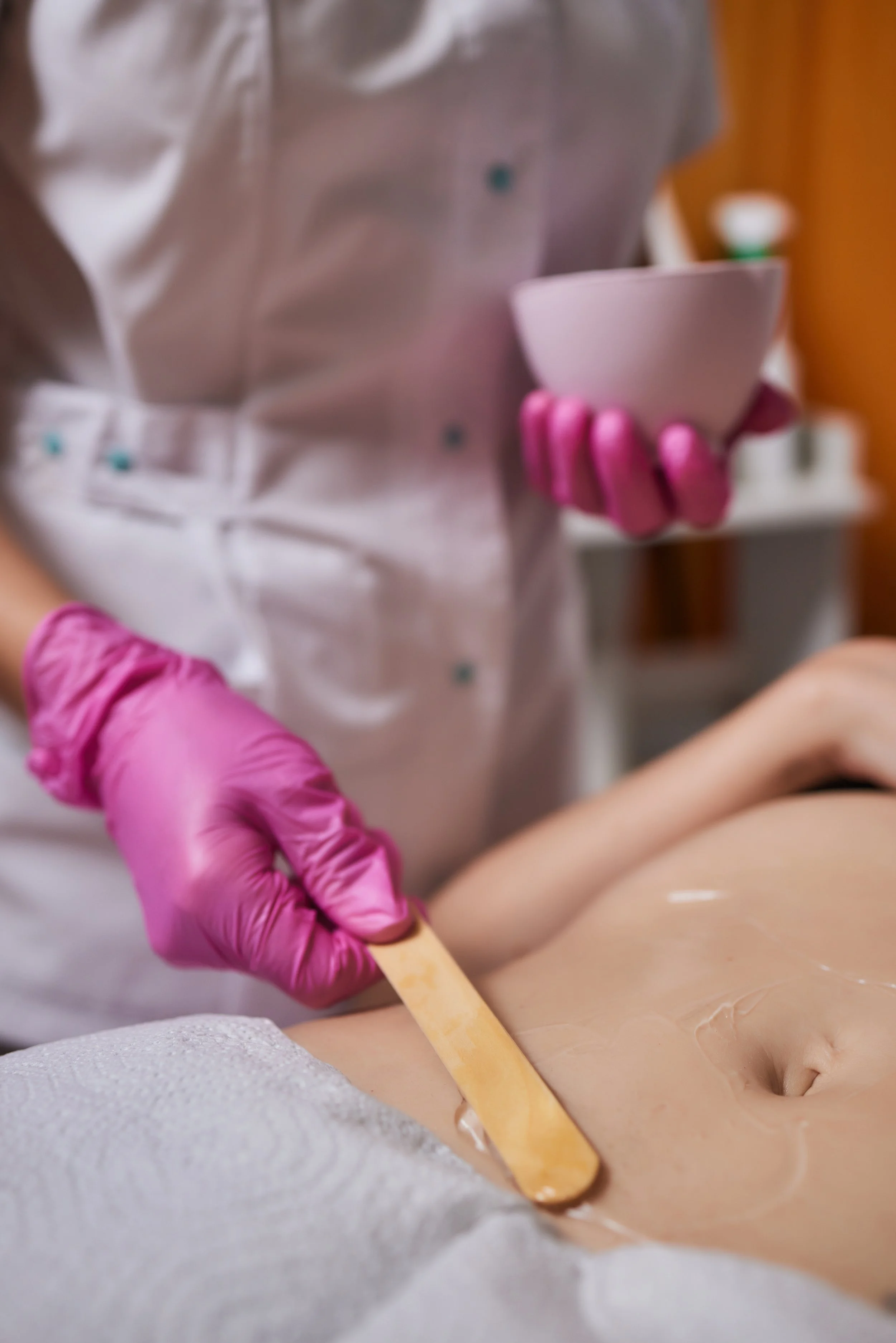 Professional esthetician applies hard wax using a wooden spatula during bikini waxing treatment.