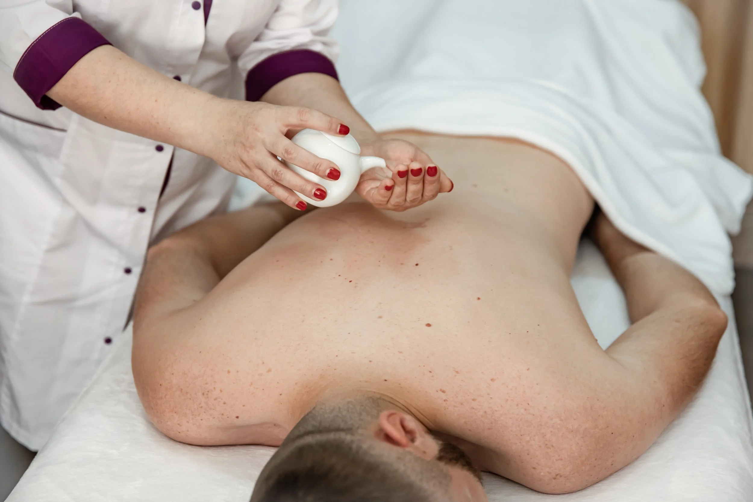 Technician applying soft wax to man’s back during waxing treatment