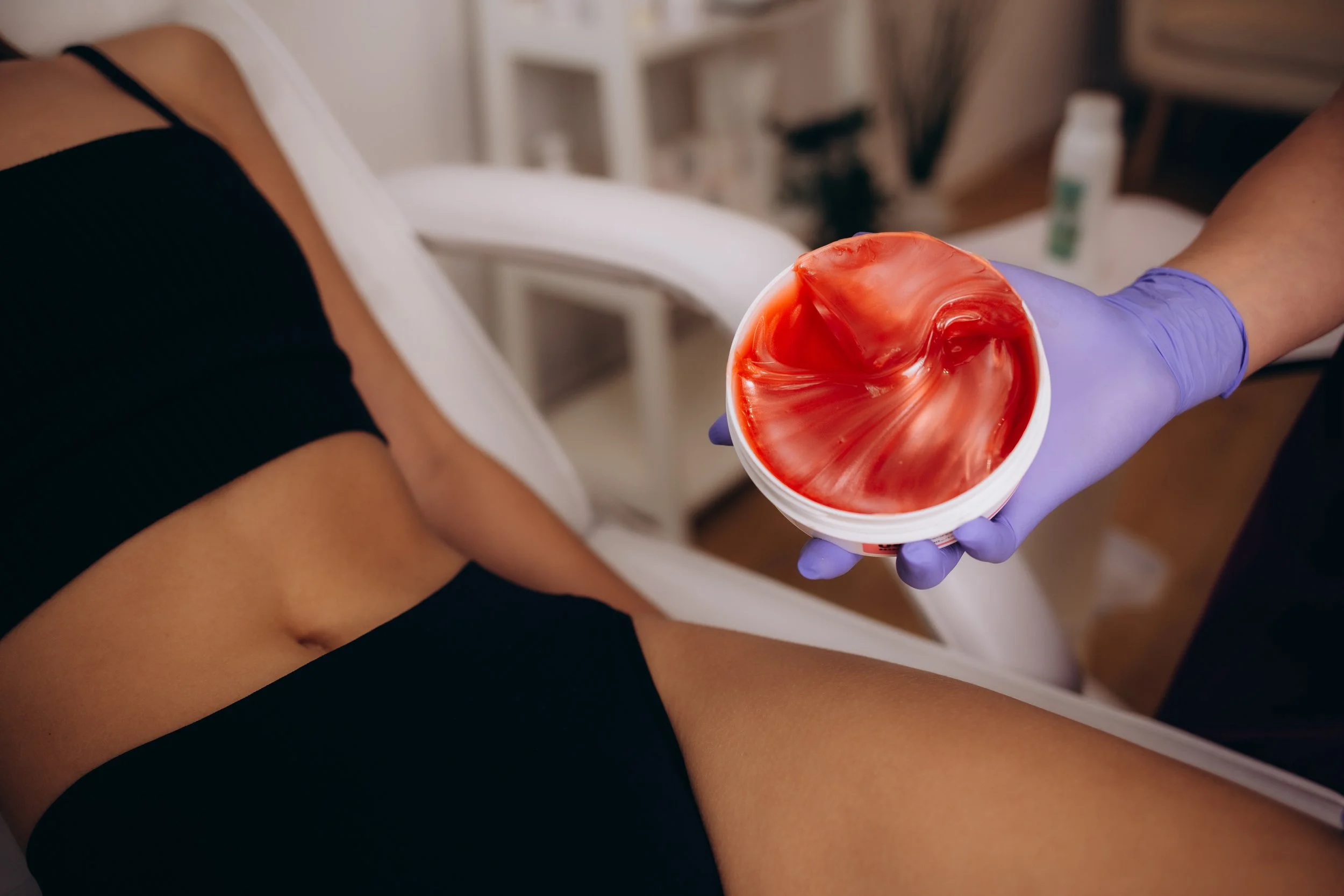 Hard wax in a container held by a gloved hand, ready for Brazilian and underarm waxing.