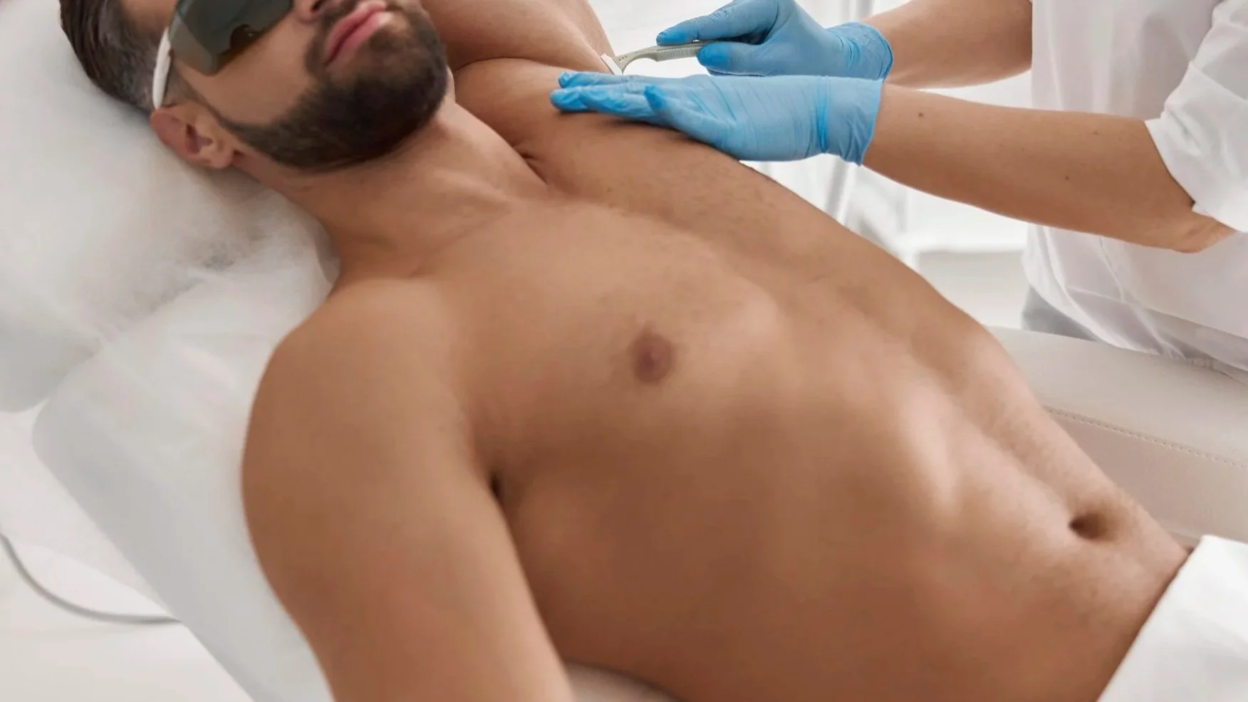 Male client receiving underarm waxing treatment with hard wax, lying on treatment table