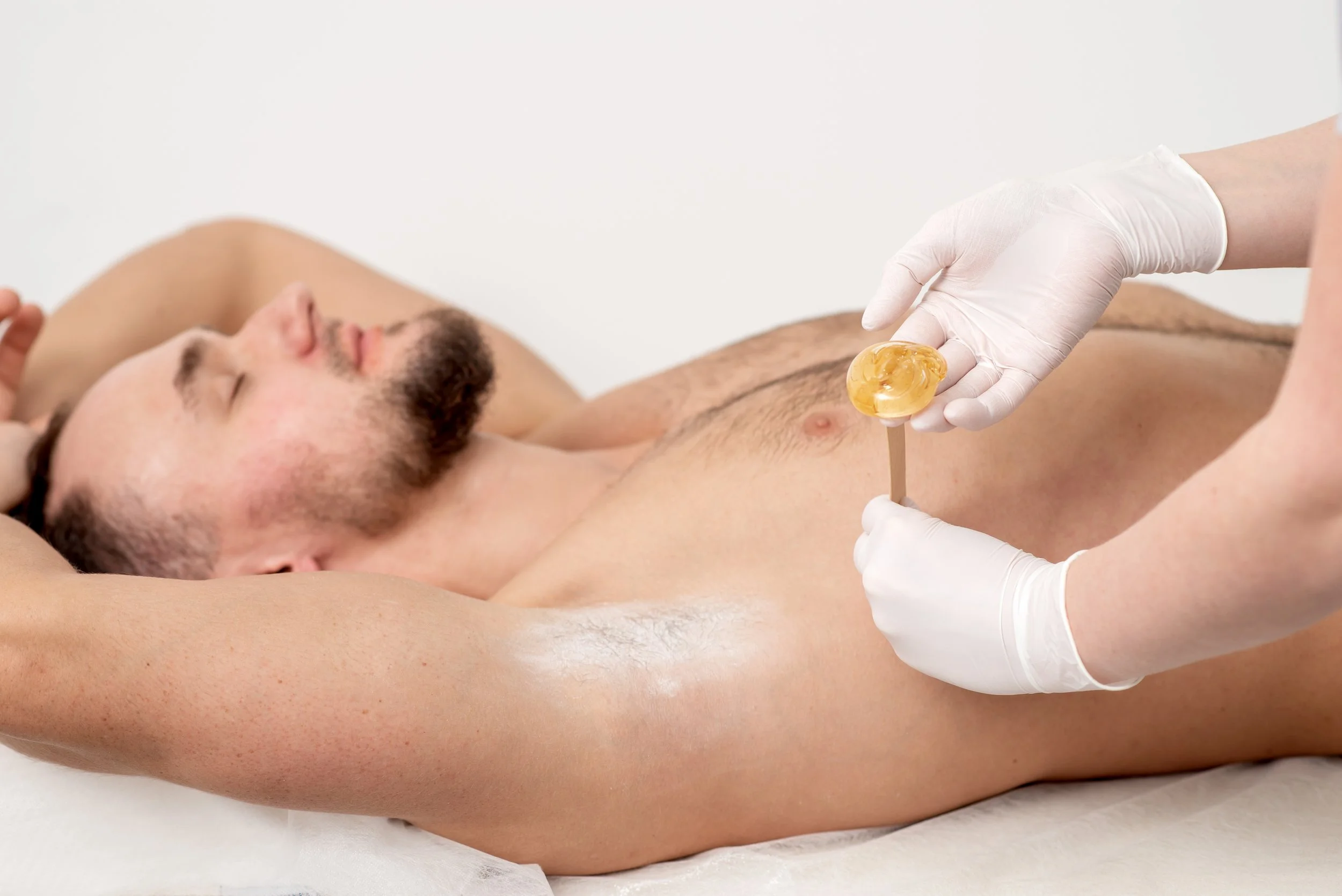 Underarm hair removal using hard wax, male client lying down.