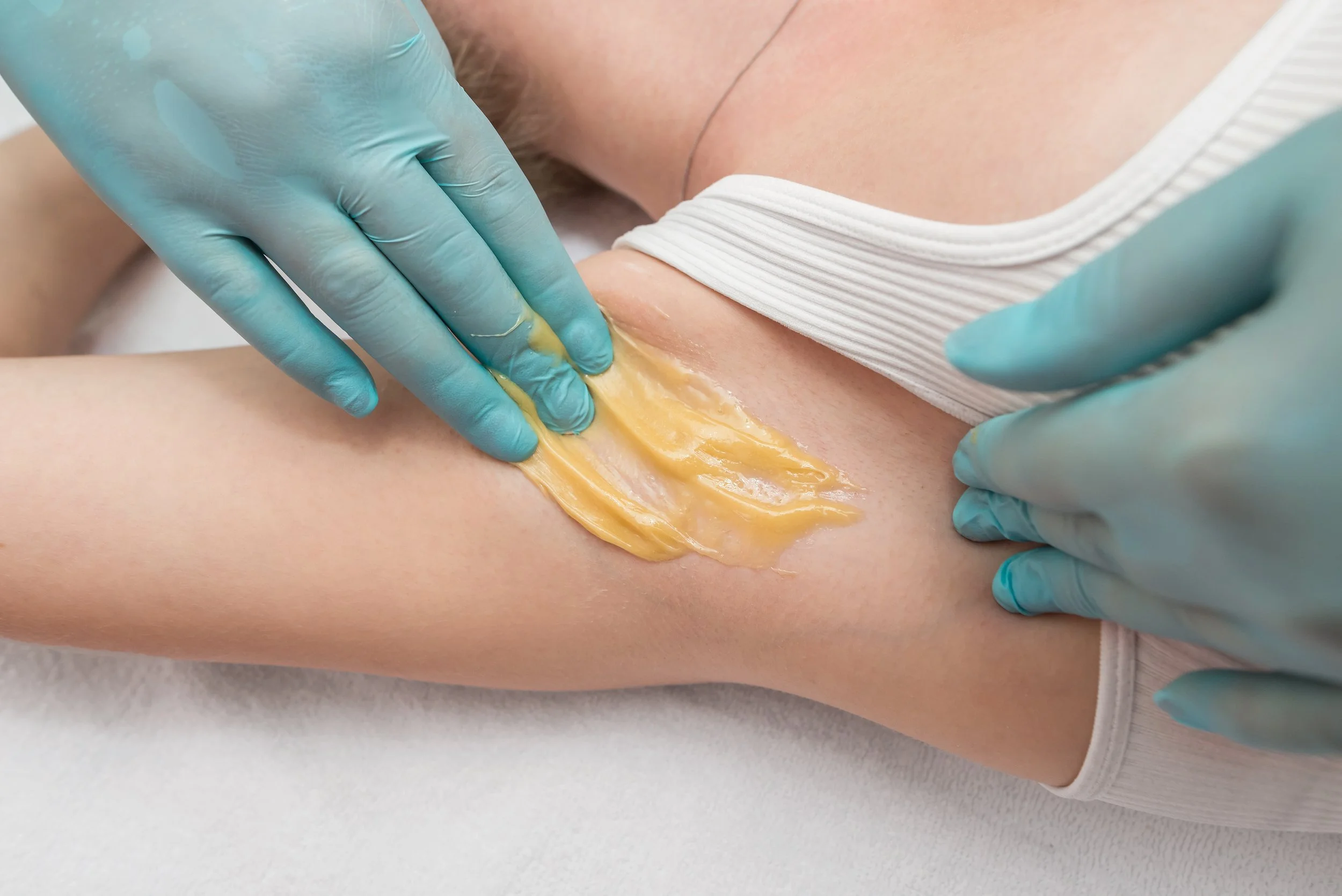 Esthetician applies hard wax to underarm area using gloved hands