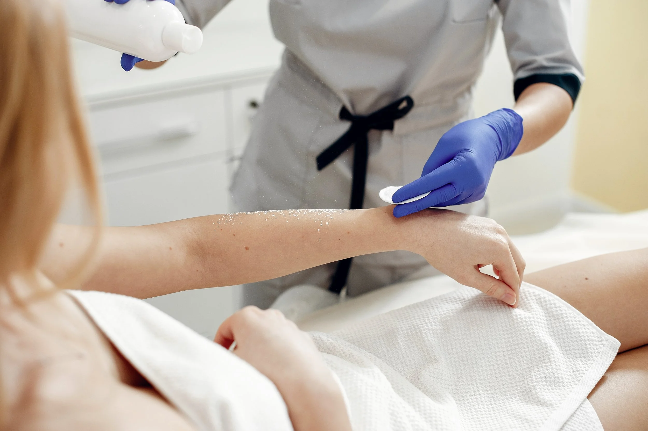 Professional applying disinfectant to client’s arm post-waxing, wearing blue gloves.