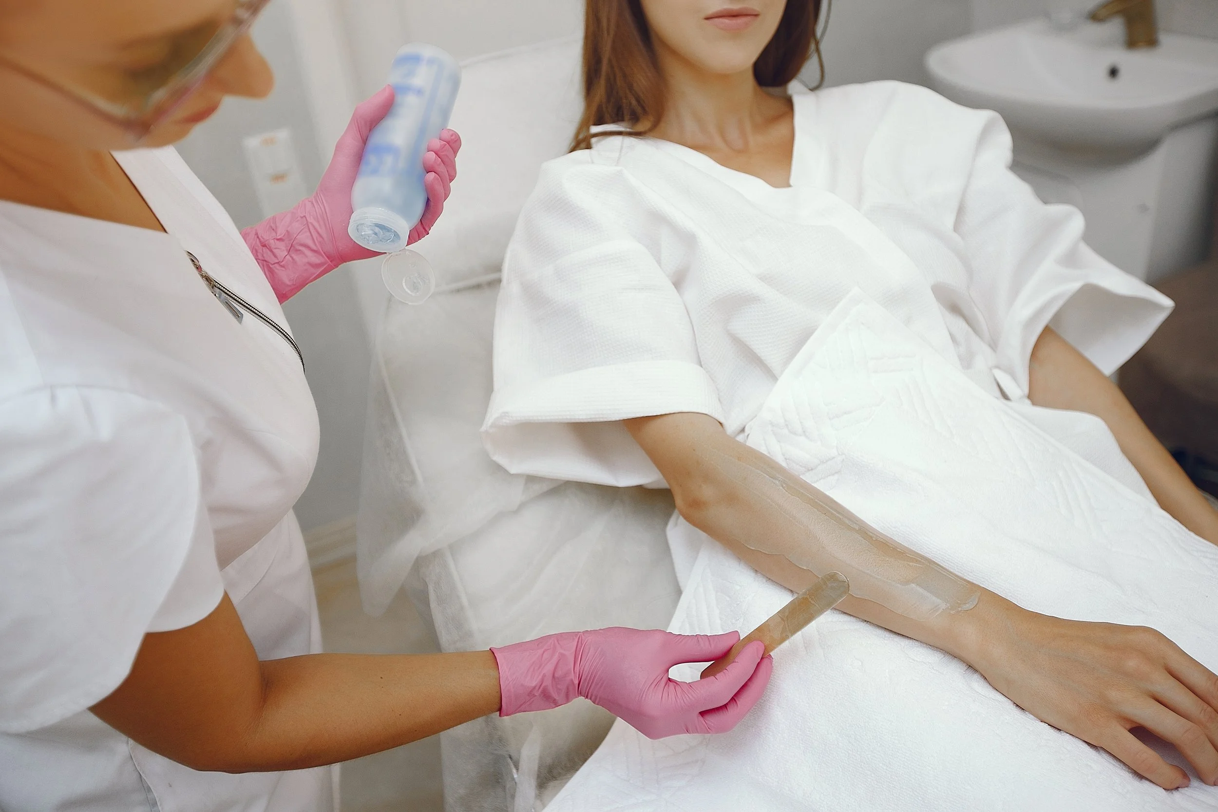 Waxing procedure on half arm: professional in white uniform and pink gloves