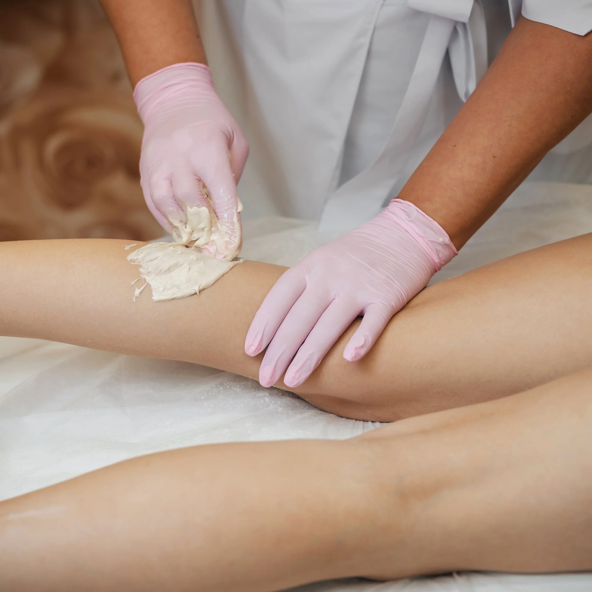 Leg waxing service: esthetician uses wax on client’s leg