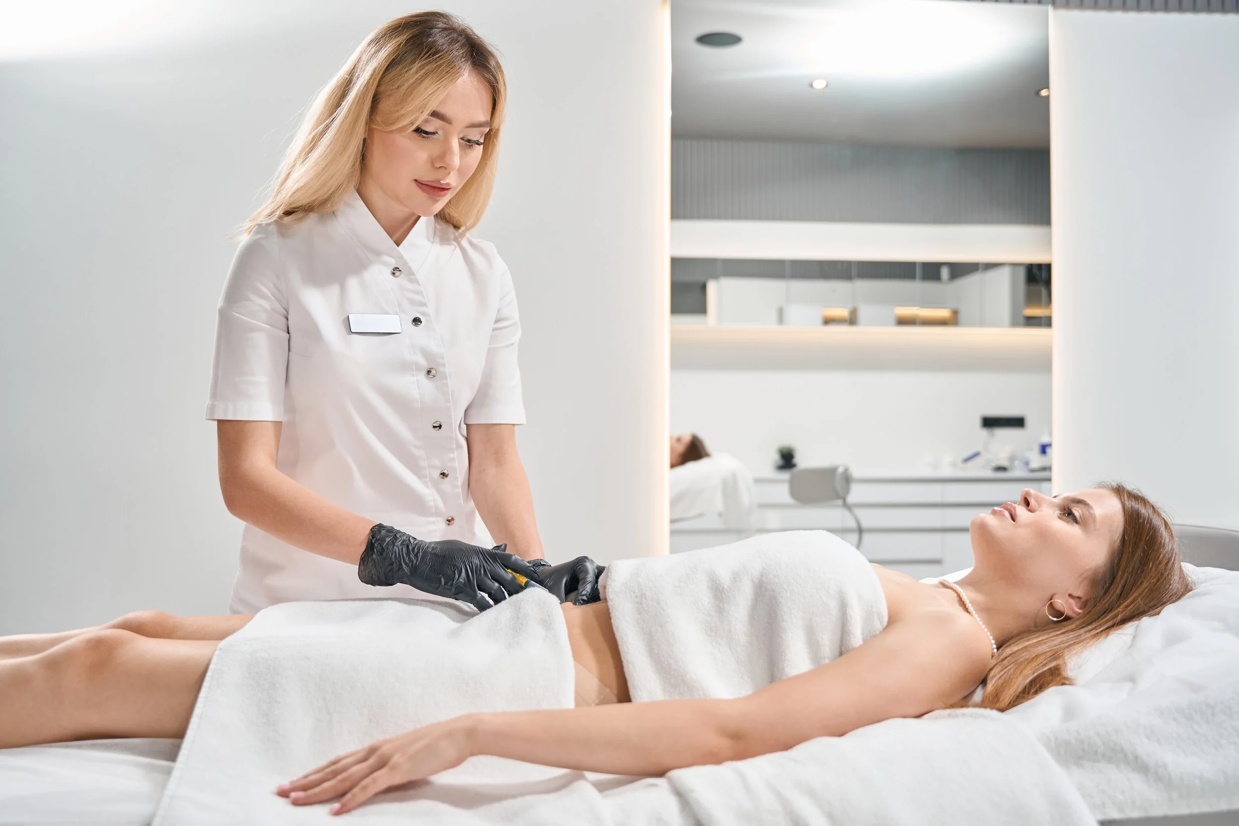 Cosmetologist performing stomach waxing on client in spa setting
