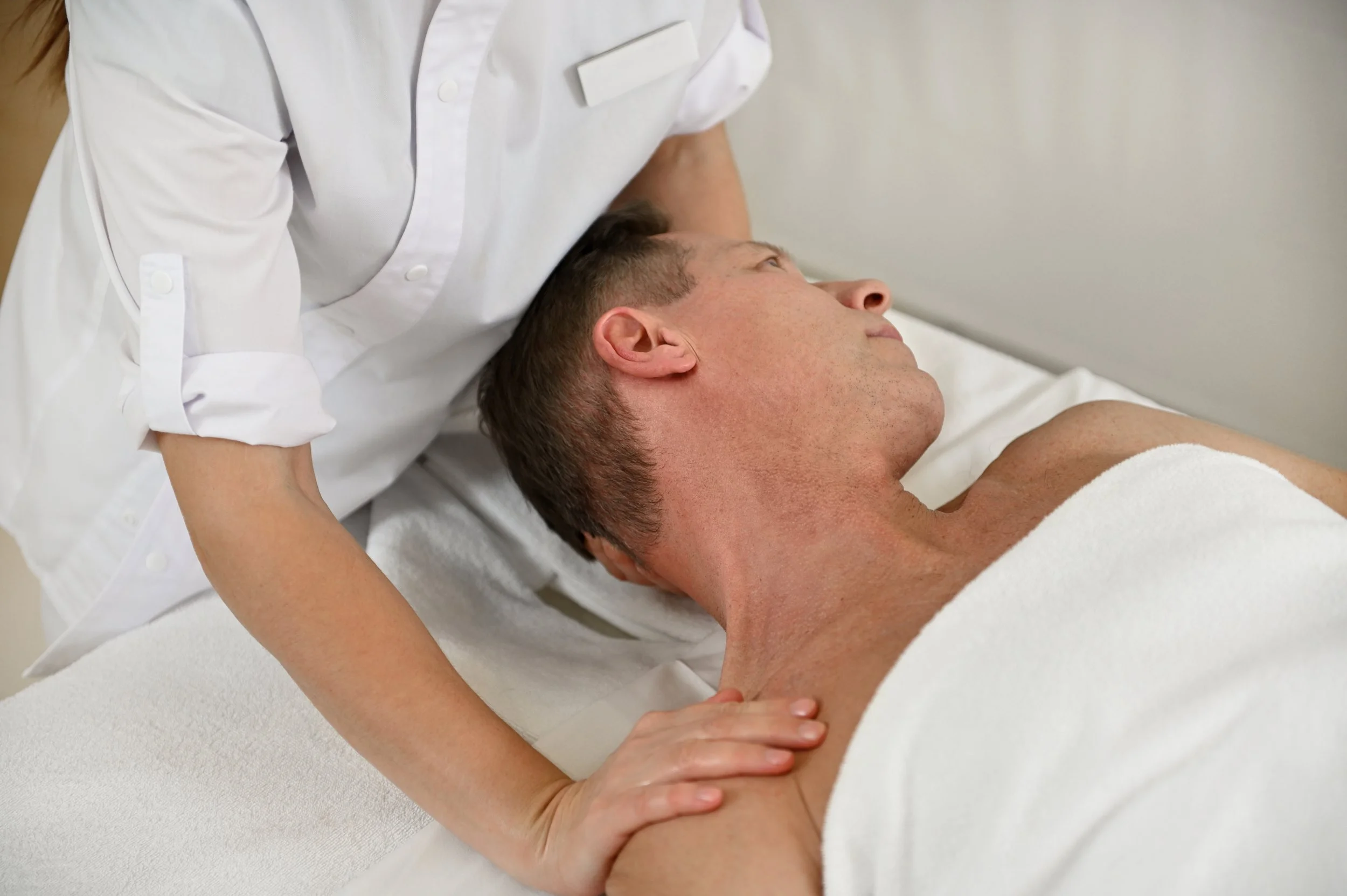 Shoulders waxing client in relaxed position, covered with towel, soft wax method