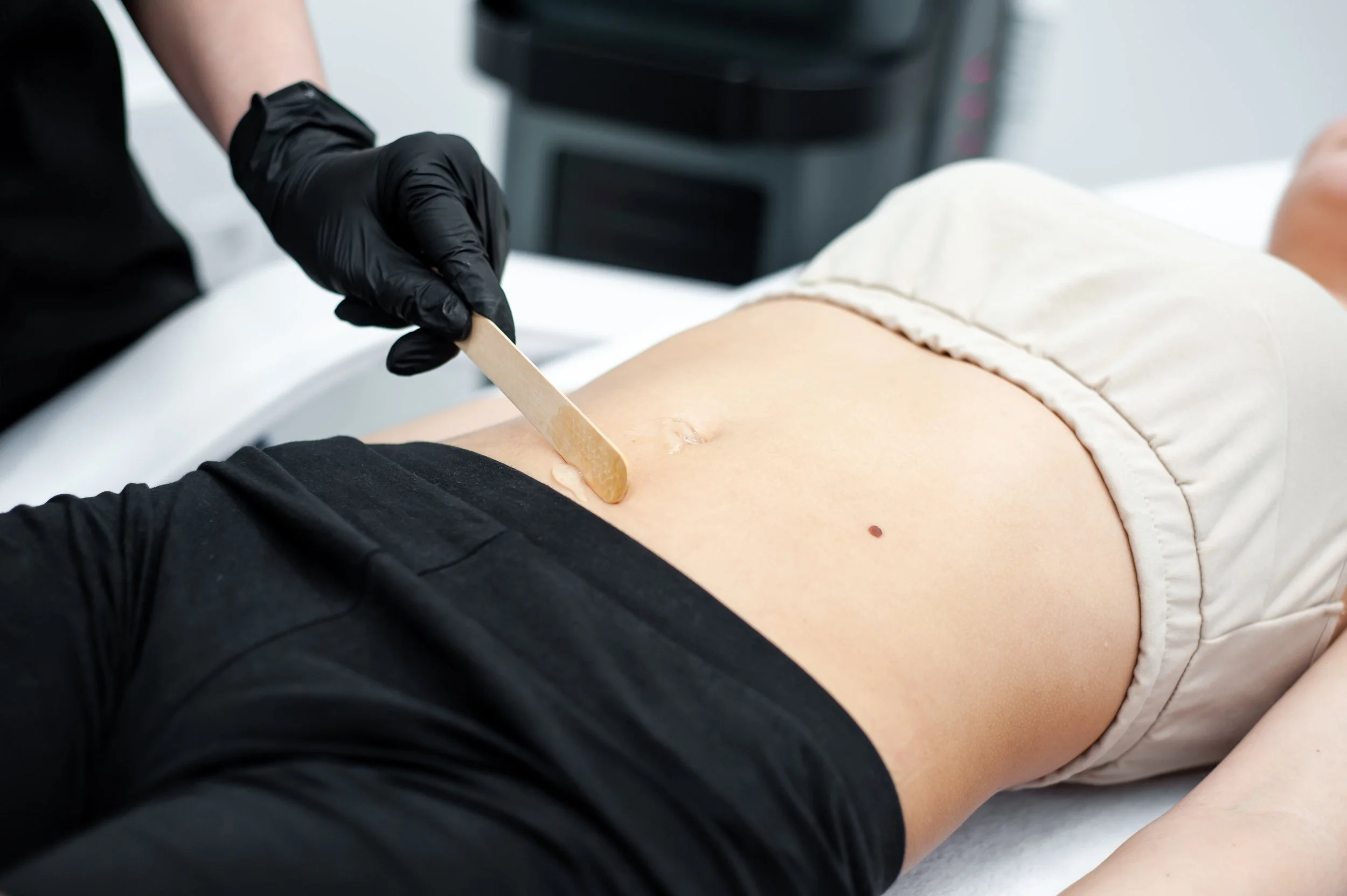 Professional applying wax to stomach using wooden spatula.