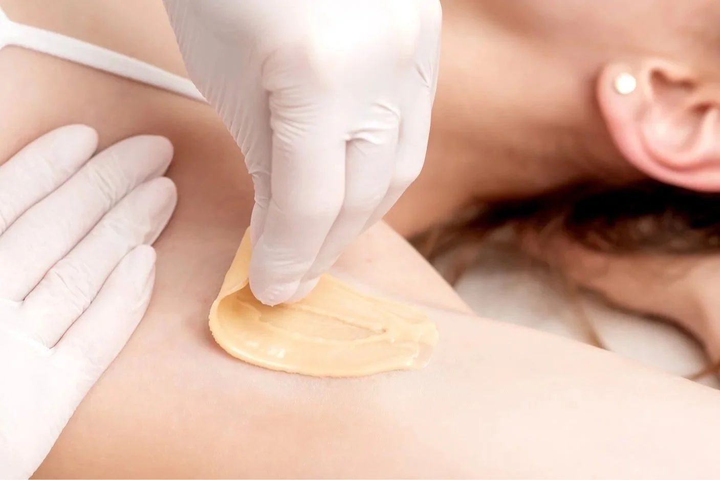 Hard wax being spread on underarm skin during professional waxing.