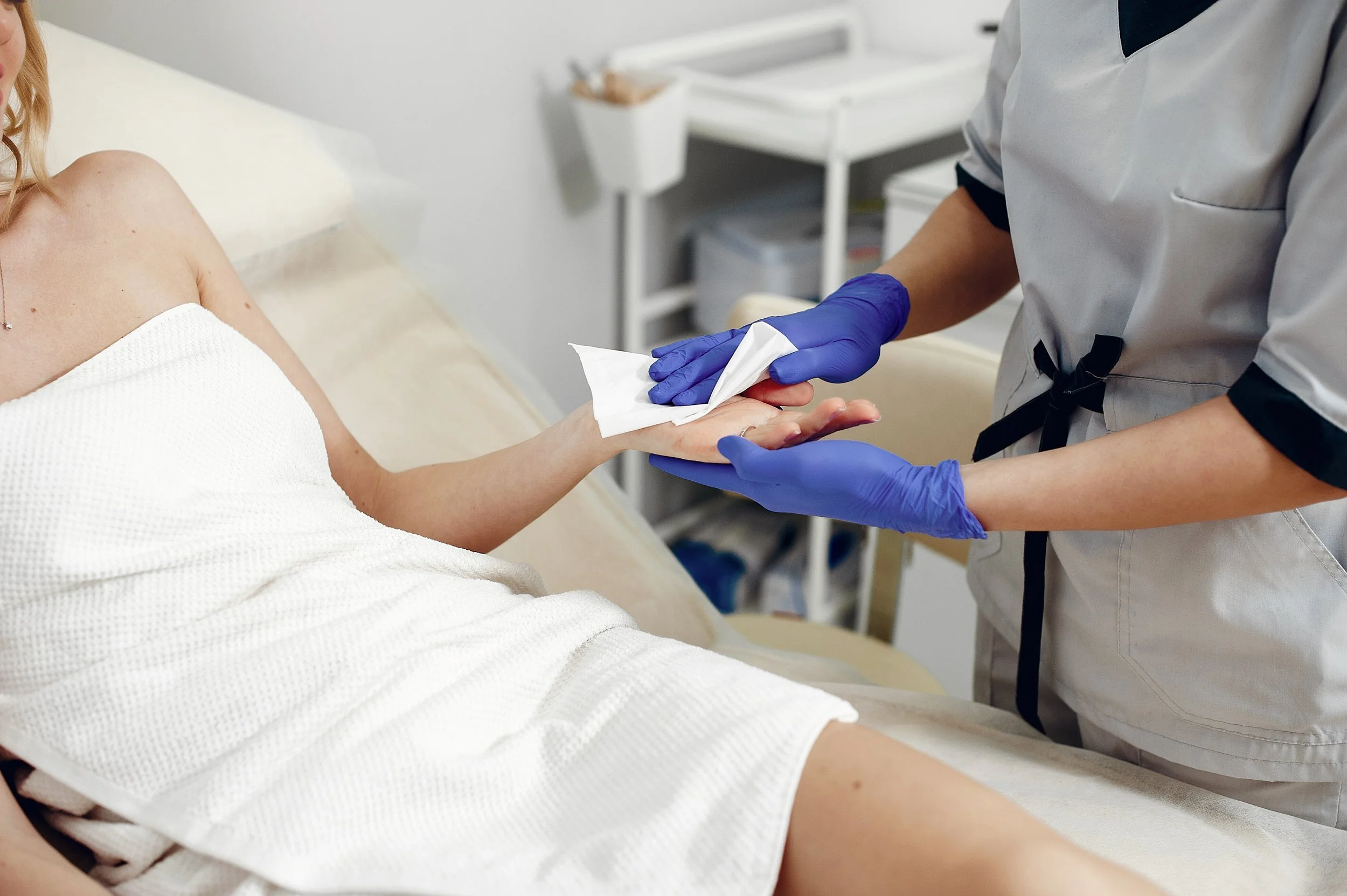 Esthetician in blue gloves applying antiseptic to client’s half arm.