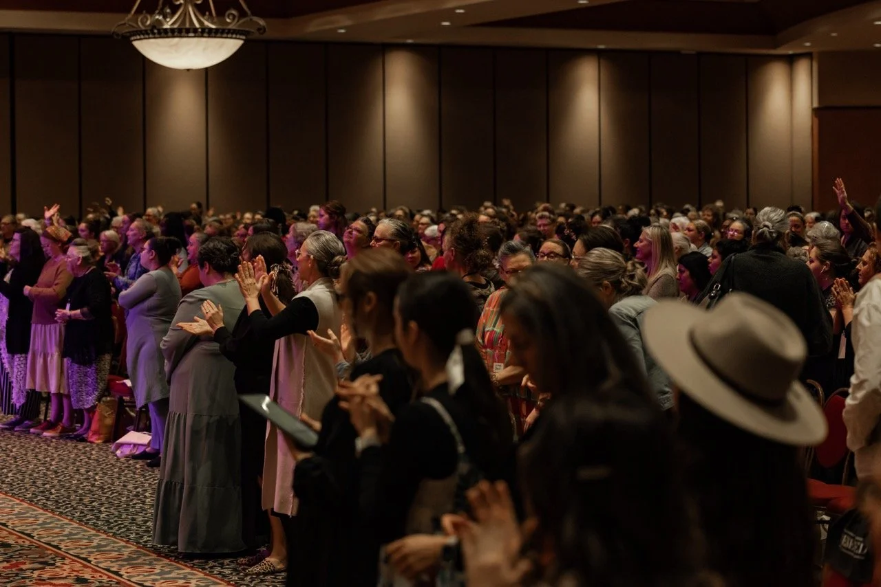 Large crowd of people standing in a conference room, some with hands raised, participating in an event.