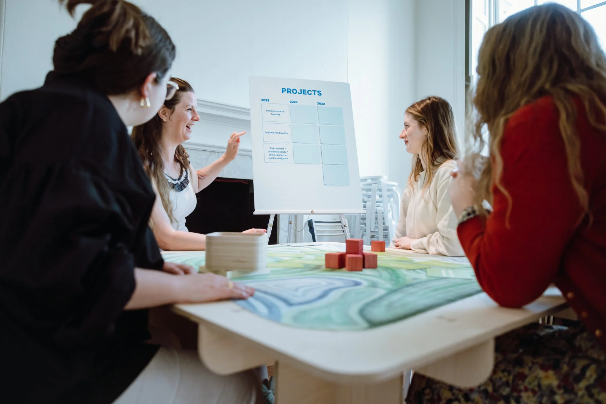A group of people around a table smiling, one points at a 'projects' board.