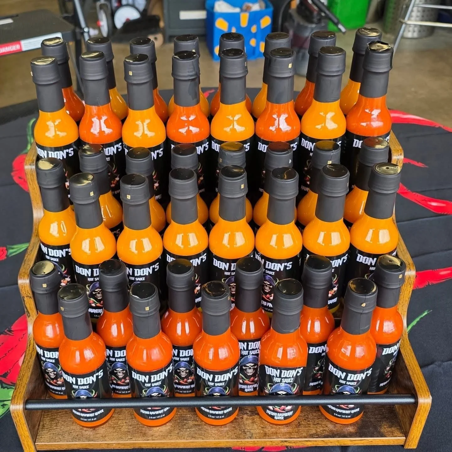 A display of hot sauce bottles labeled 'Don Don's', arranged on a wooden tray with a black cloth featuring a red and green design underneath.