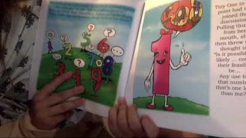A person holding a children's book, showing a colorful page with numbers and a cartoon character with a pink body and red hair.