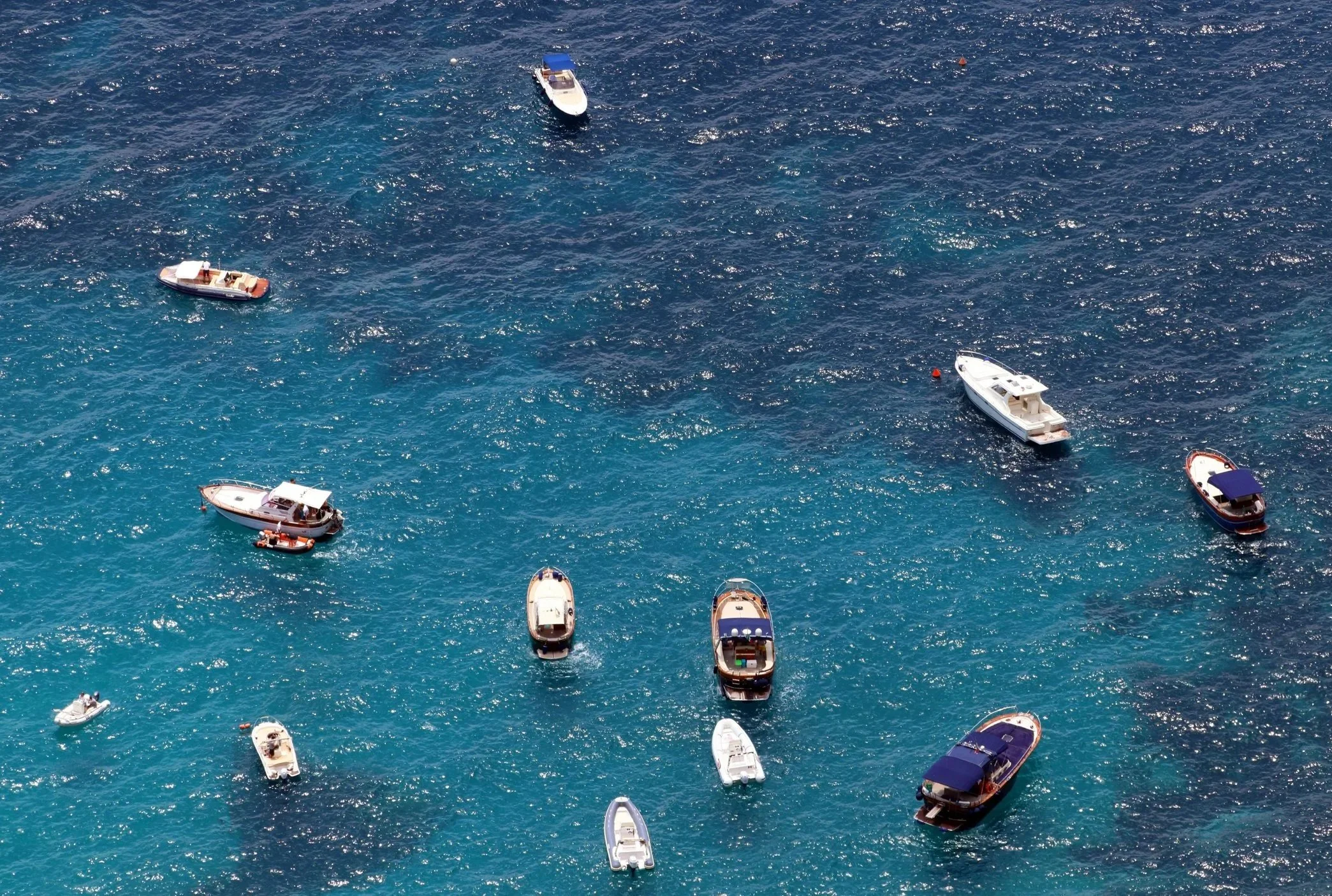 Multiple boats anchored on clear blue water, viewed from above.
