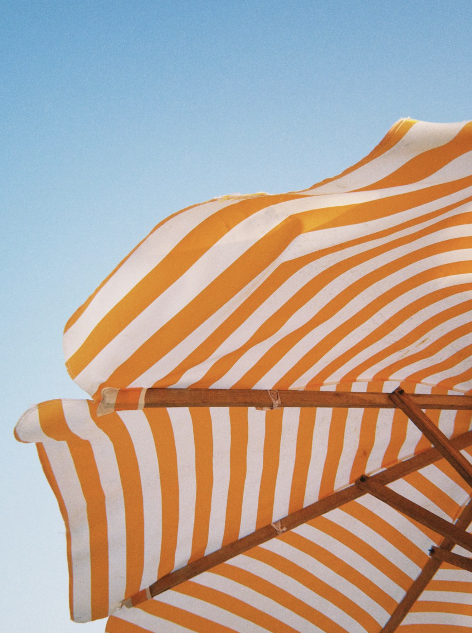 A yellow and white striped beach umbrella against a clear blue sky.