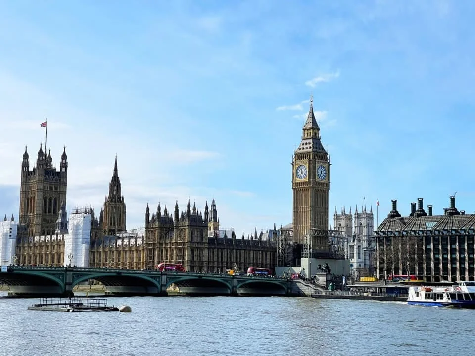 London's Big Ben clock tower and the Houses of Parliament along the River Thames, with a bridge and boats in the foreground.