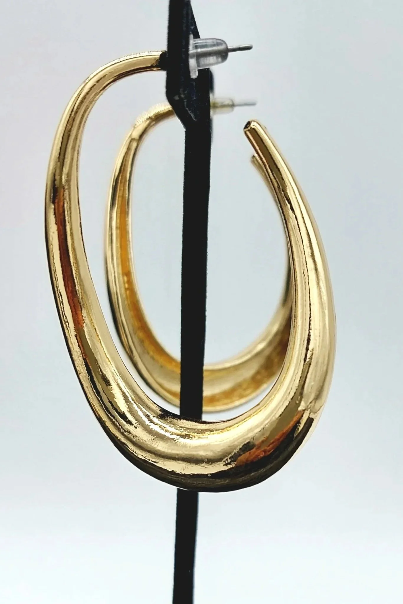 A pair of gold hoop earrings hanging from a black display stand against a plain background.
