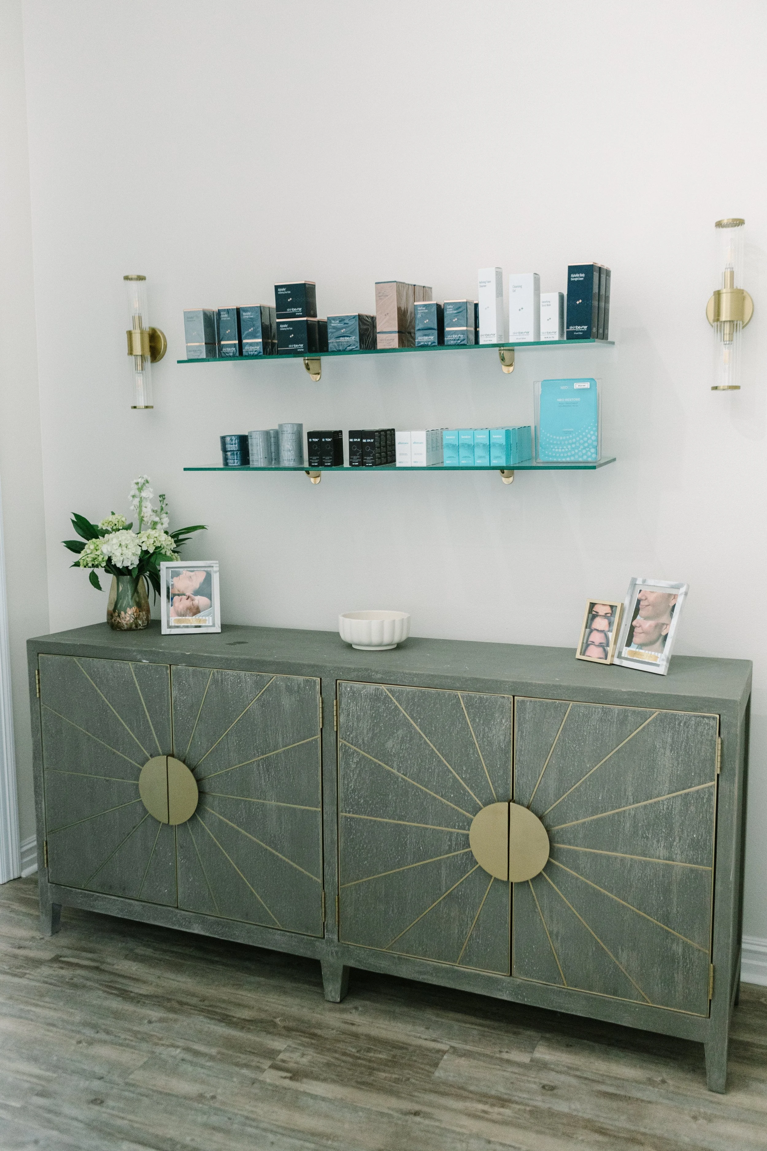 A gray-green sideboard against a light-colored wall with two glass shelves holding skincare products.