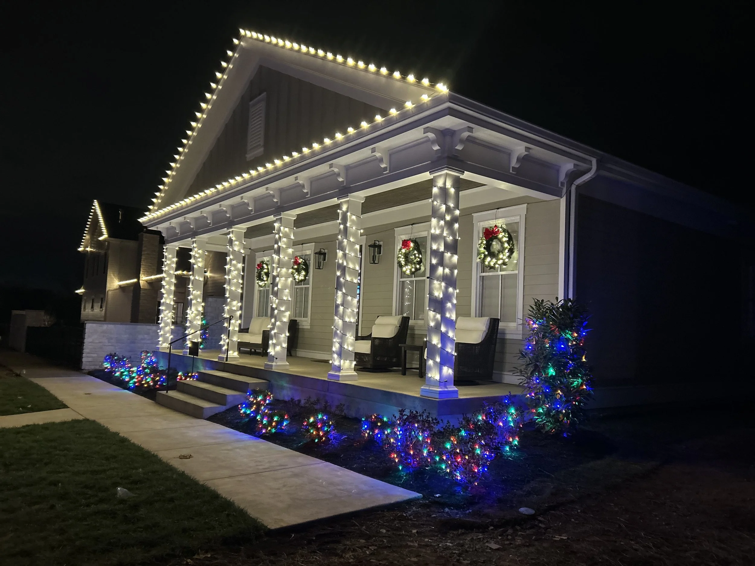 A large brick house decorated with string lights outlining the roof at night.