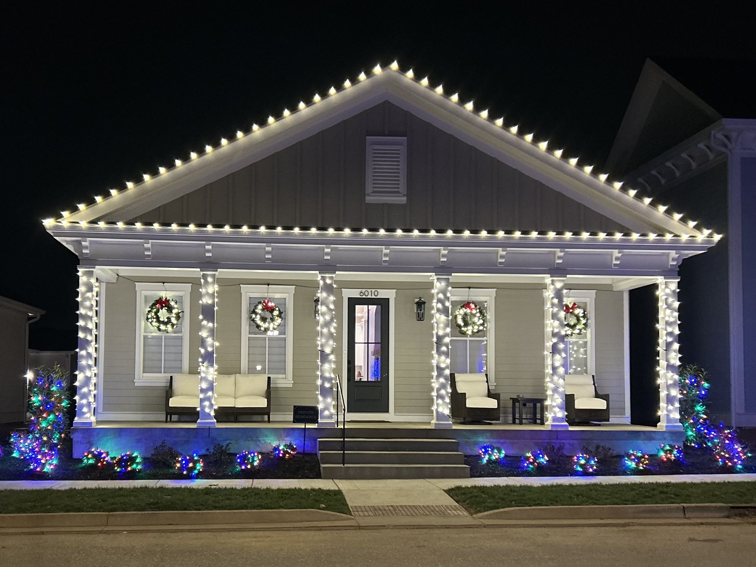 A large brick house decorated with string lights outlining the roof at night.