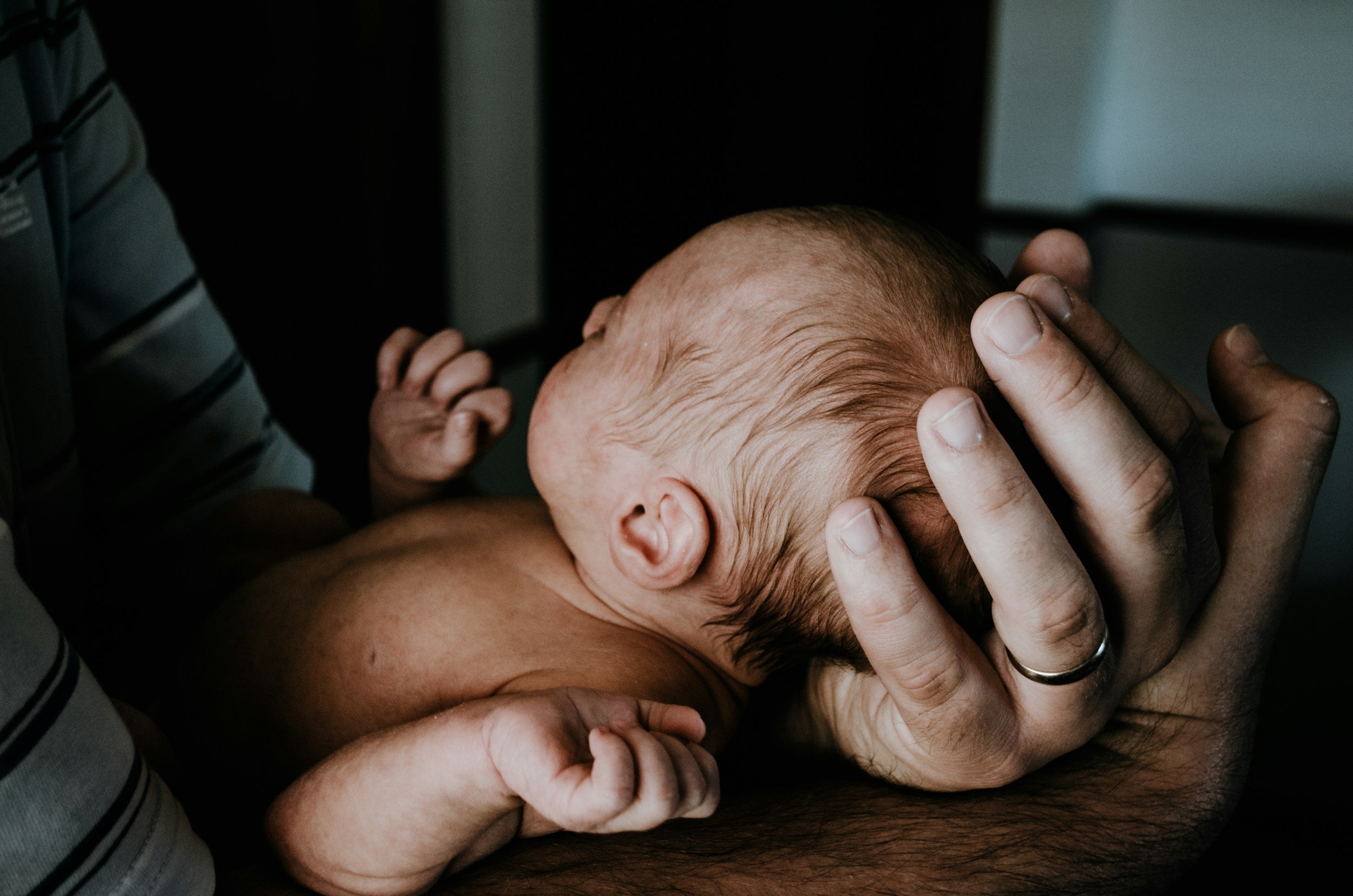 A newborn baby being cradled and gently held by an adult. The focus is on the baby's head and hand as the adult supports the baby's head.