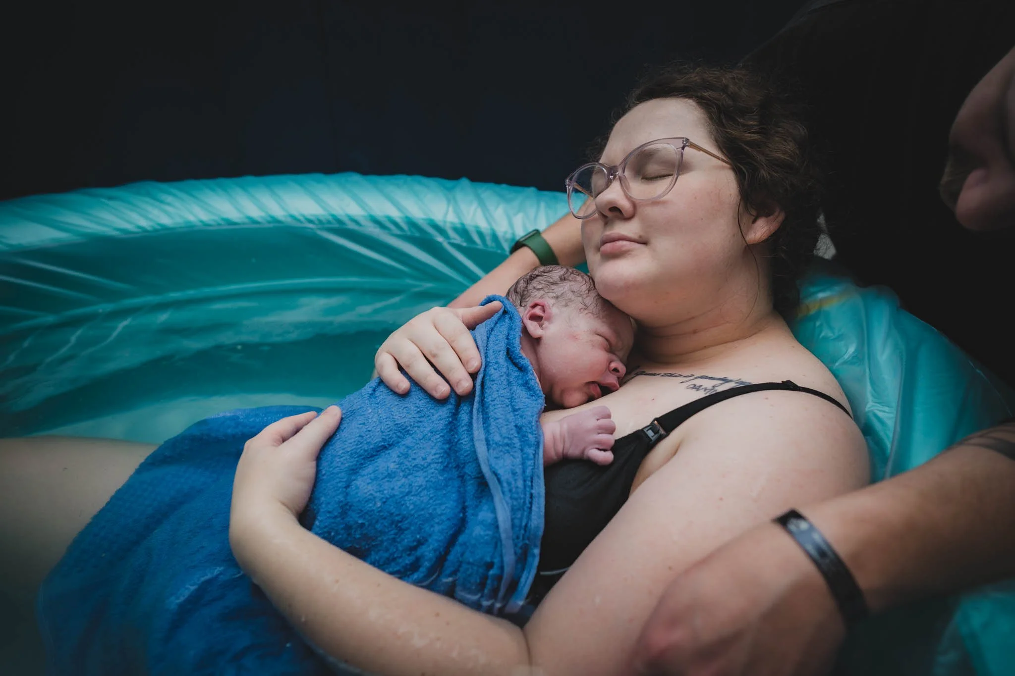 A woman giving birth to a newborn in a birthing pool, holding the baby close to her chest with a peaceful expression.