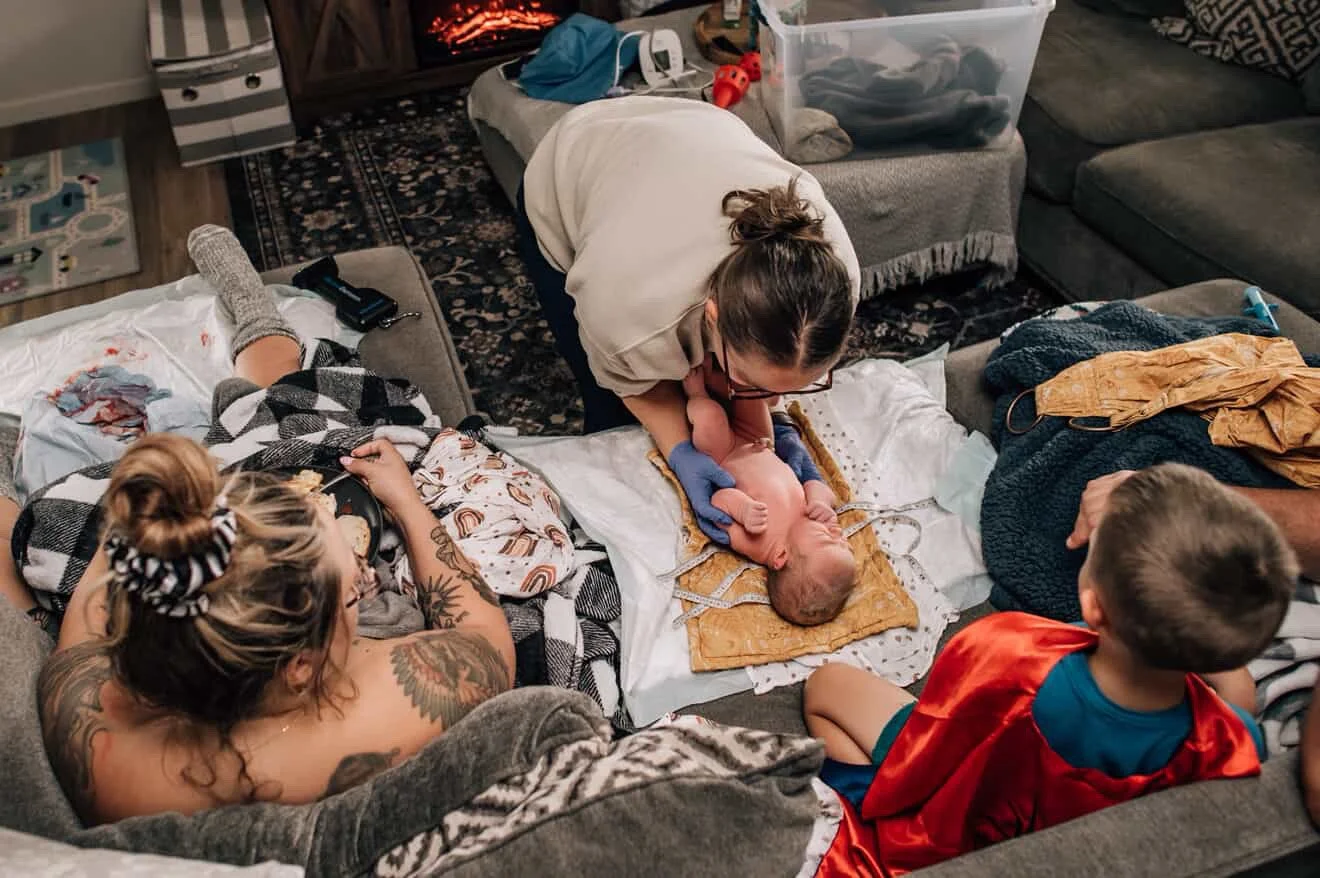 A woman and children helping deliver a newborn on a couch in a living room.