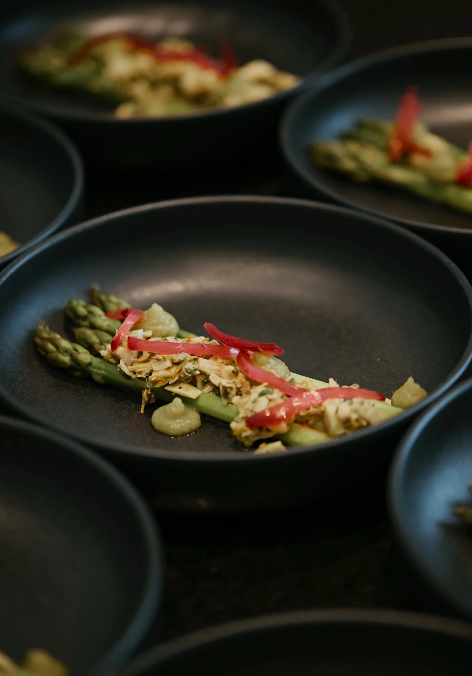 Assiette avec asperges, garnie de graines et de sauce rouge.