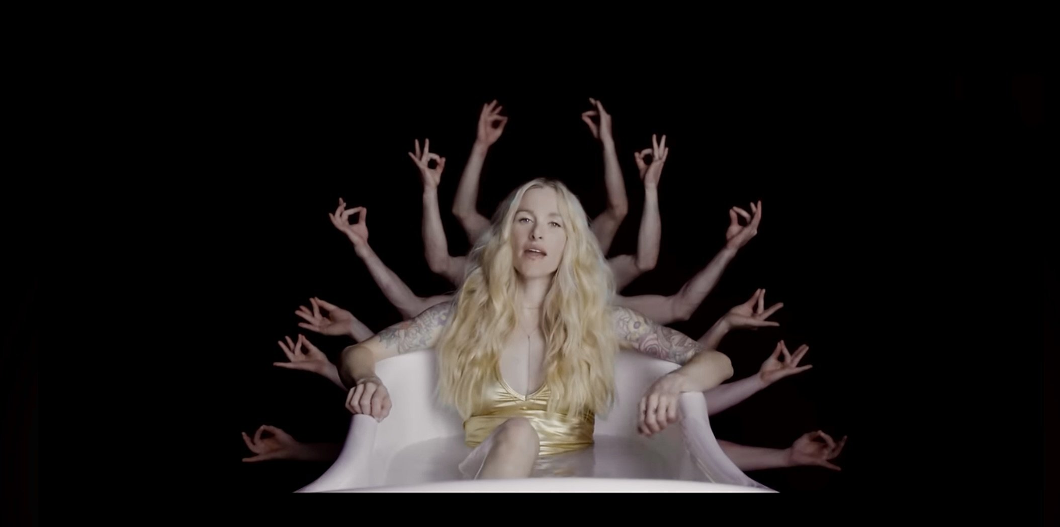 A woman with long blonde hair sitting in a white bathtub, surrounded by multiple disembodied arms making various hand gestures against a black background.