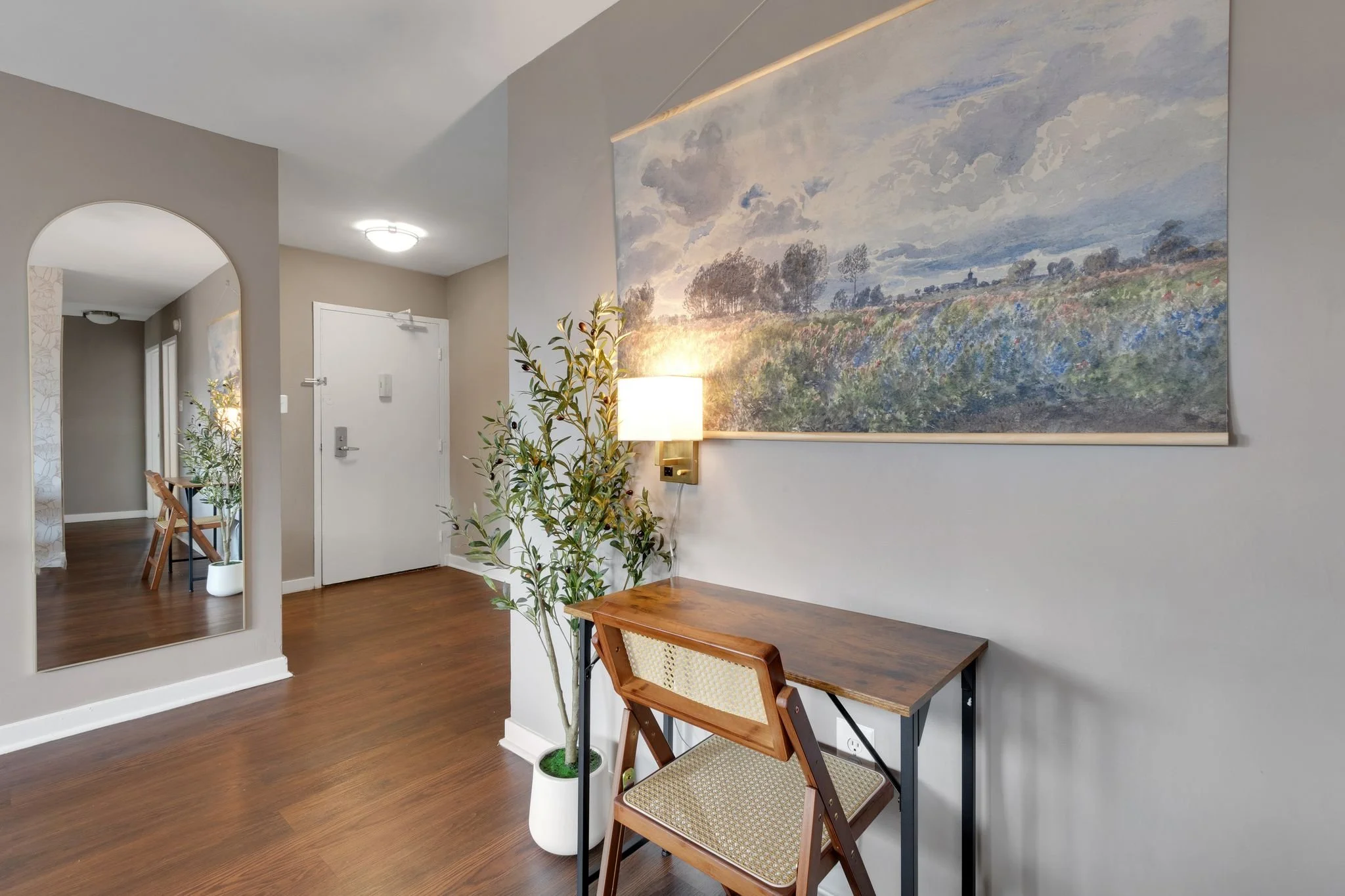 Entryway with a wooden table, a chair, a potted plant, and a large landscape painting on the wall.