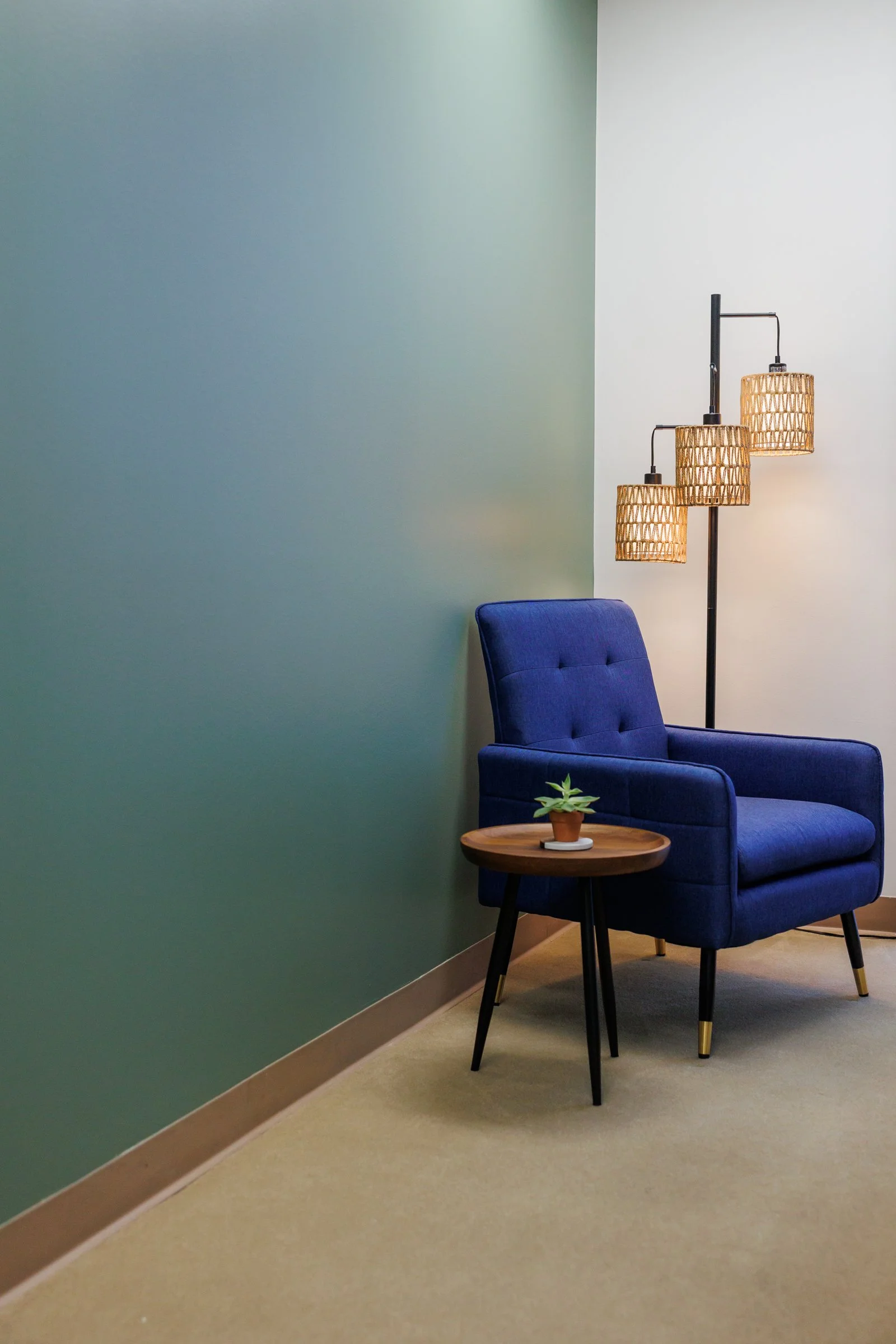 A room corner with a blue armchair, a small wooden side table with a potted plant, and a multi-shaded floor lamp with rattan lampshades.