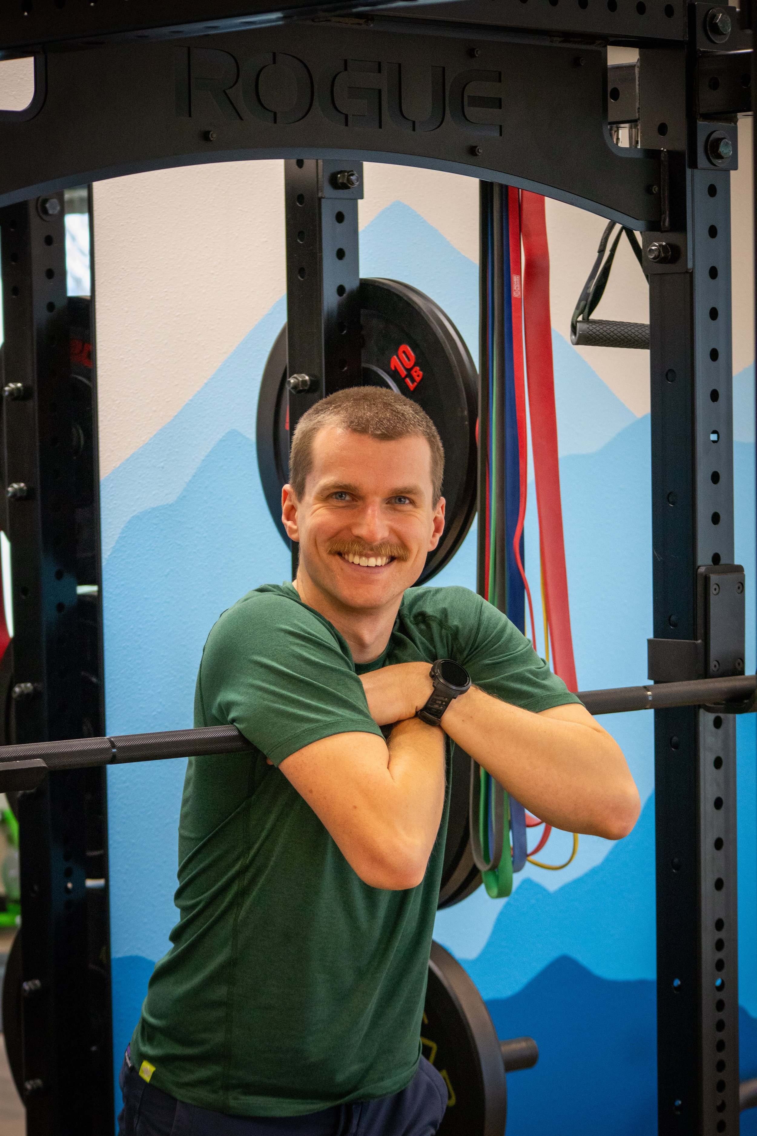 Ben Hoskyn smiling at the camera leaning over a barbell wearing a green t-shirt.