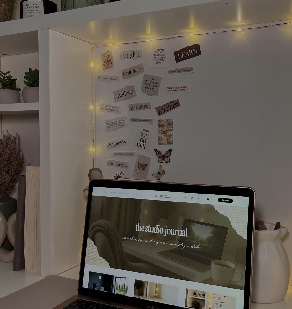 Laptop on a cosy white desk displaying the Socialuxe UK Studio Journal website, surrounded by vision board quotes, warm lighting, and autumn-inspired décor.